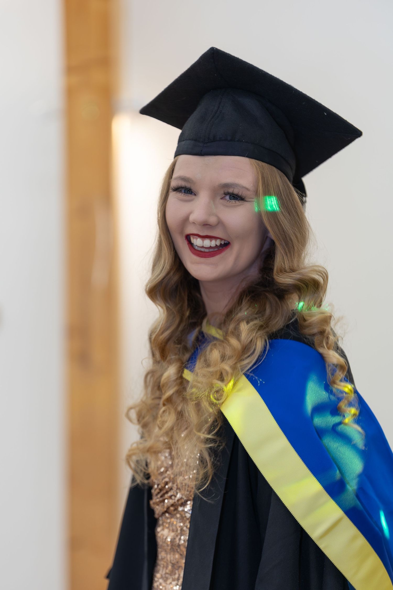 Smiling female graduate in black mortarboard cap and blue sash celebrating her graduation ceremony.