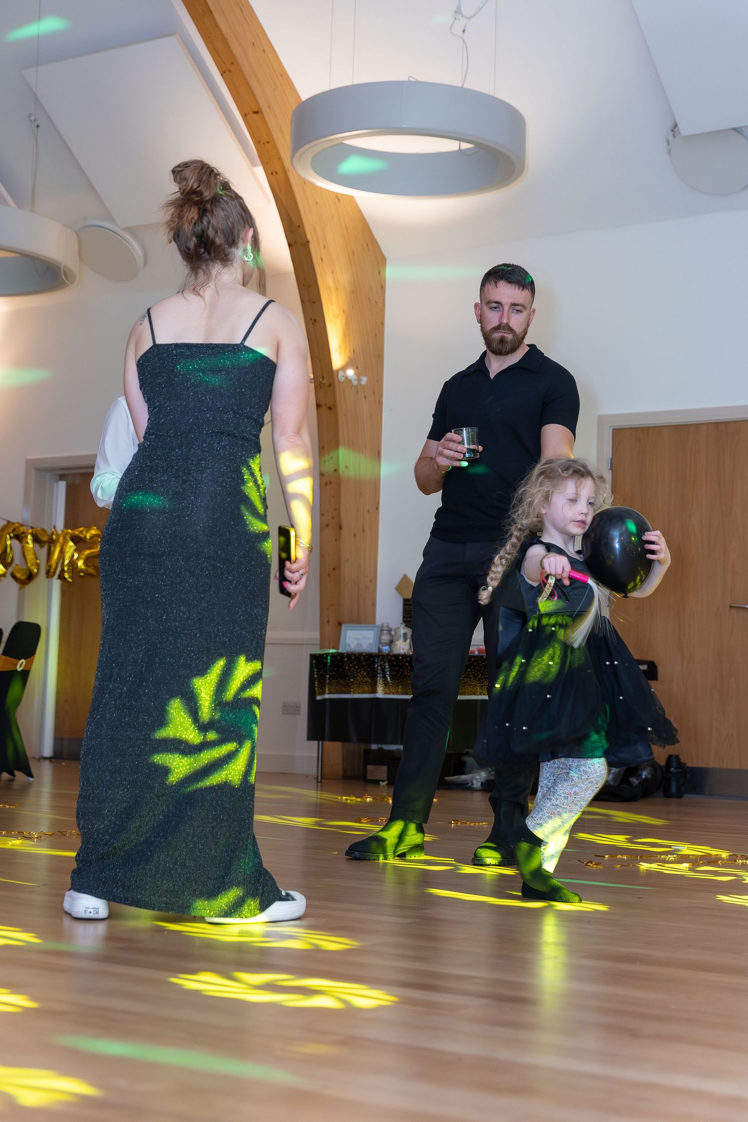 Family dancing at a party with green light projections on the floor in a modern hall.