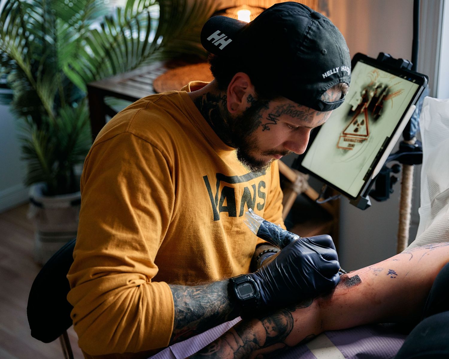 A tattoo artist in yellow sweatshirt working on a client's arm.