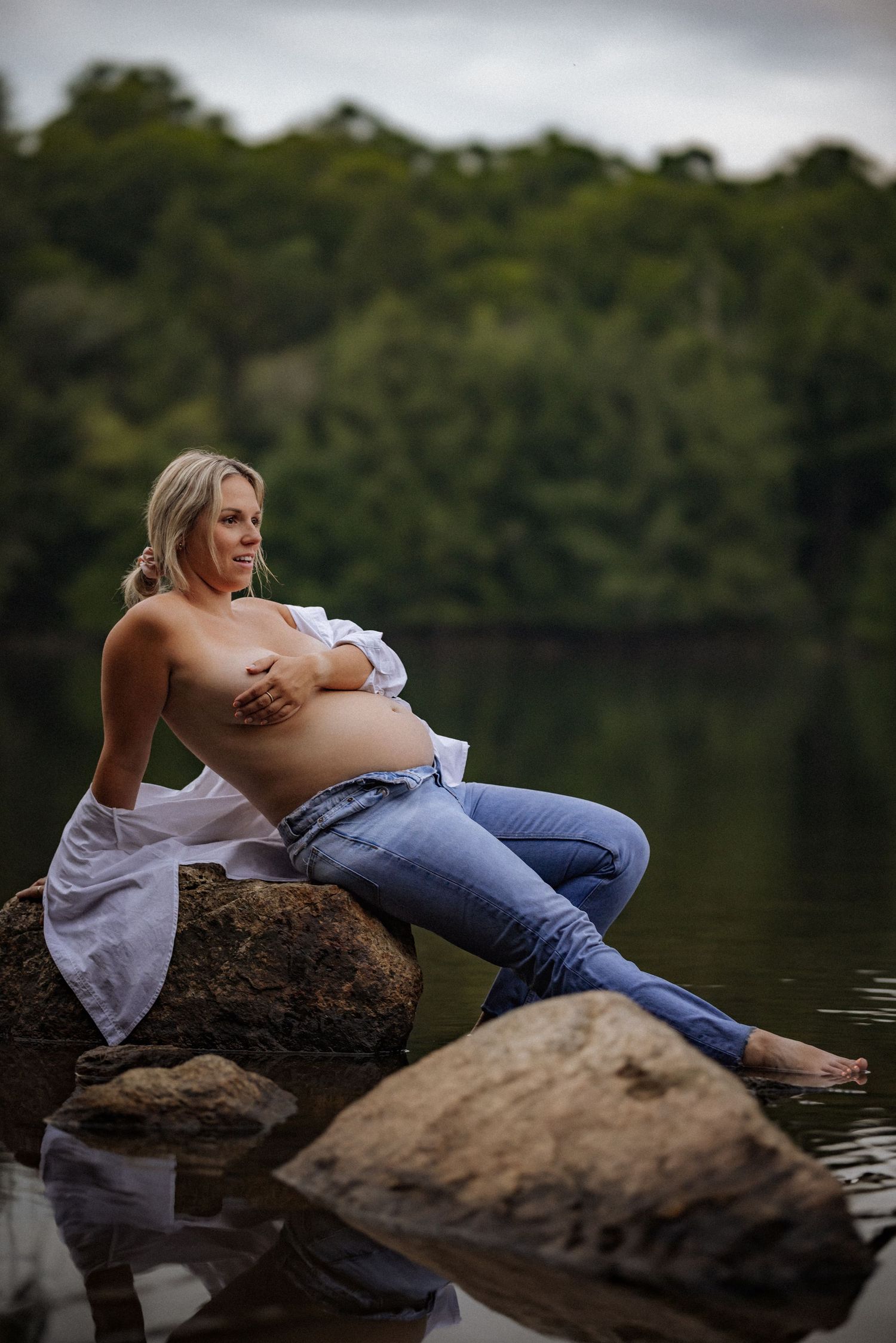 Couple relaxing on rocks by serene lakeside surrounded by nature.