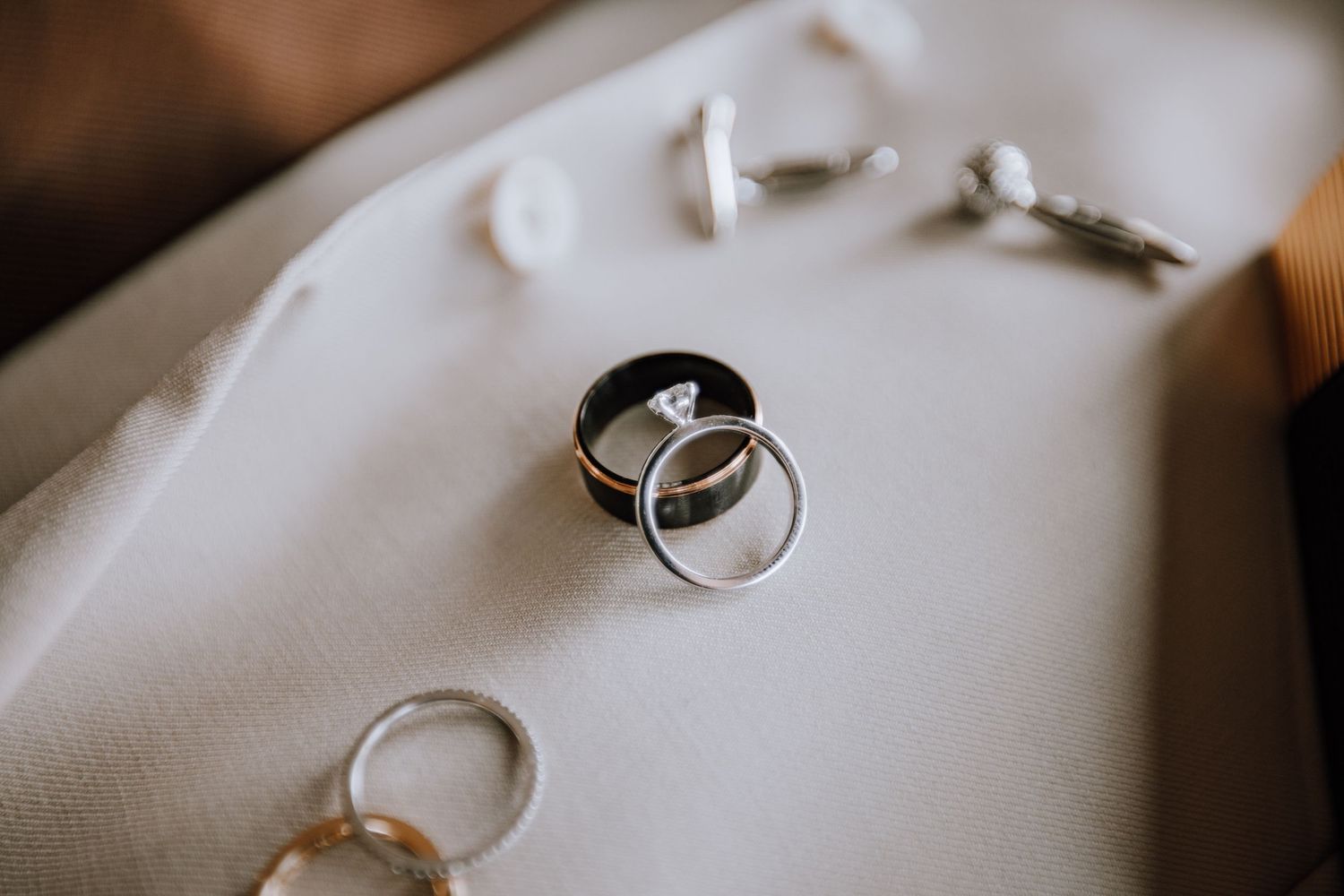 Close-up details of wedding rings and jewelry on white fabric.
