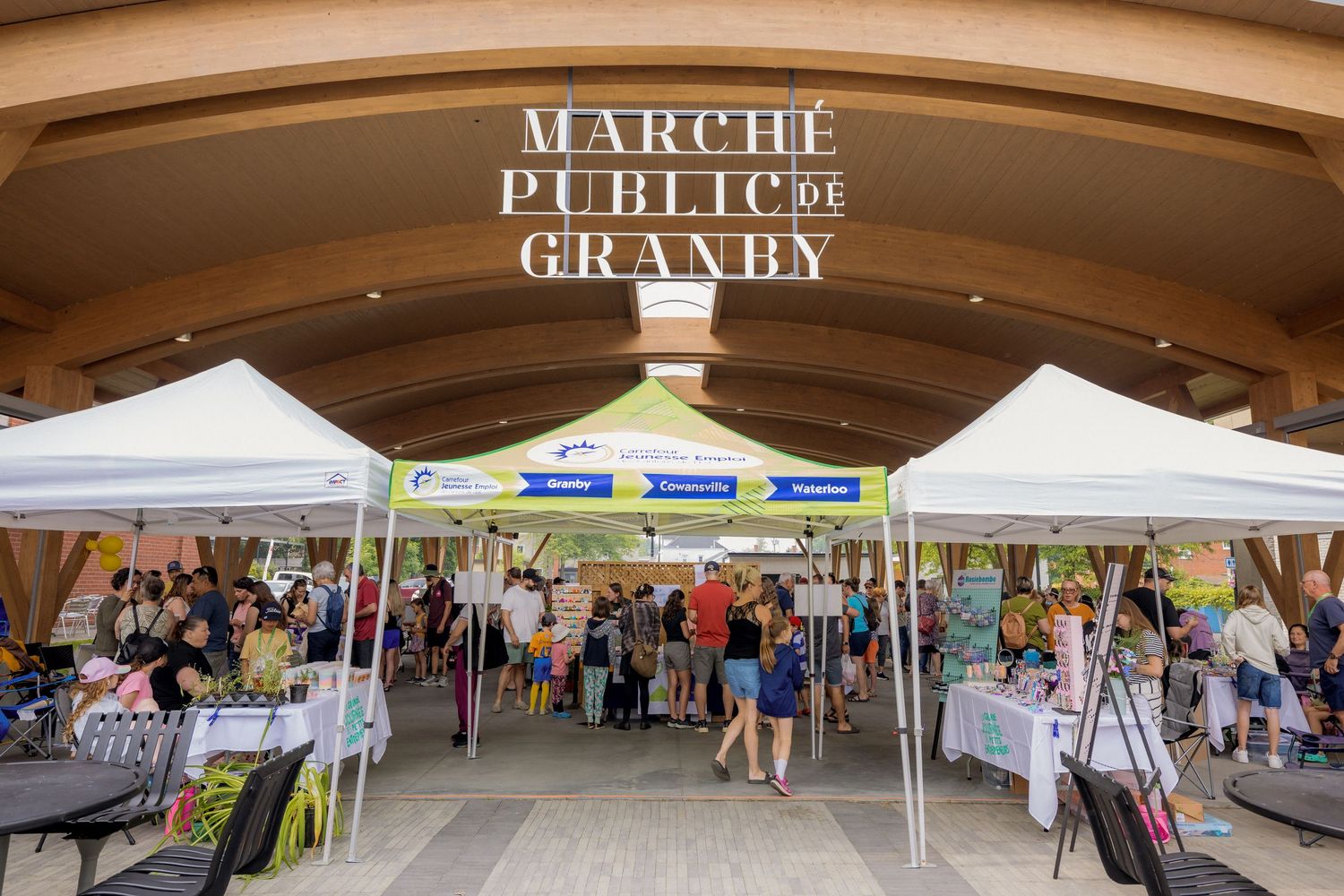 Marche Public Granby sign over outdoor market tents with shoppers browsing vendor stalls.