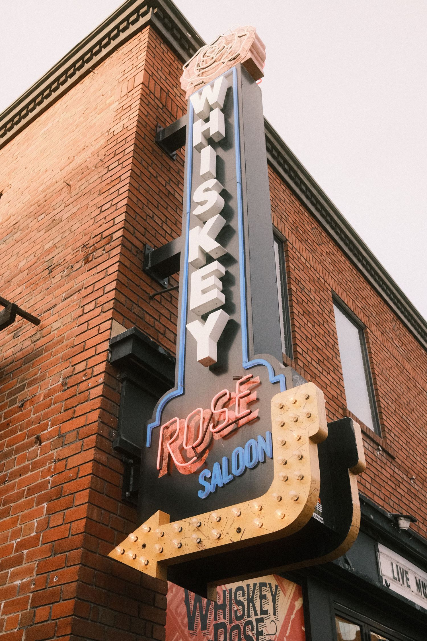 Whiskey Rose Saloon neon sign shaped like a guitar on a red brick building corner.