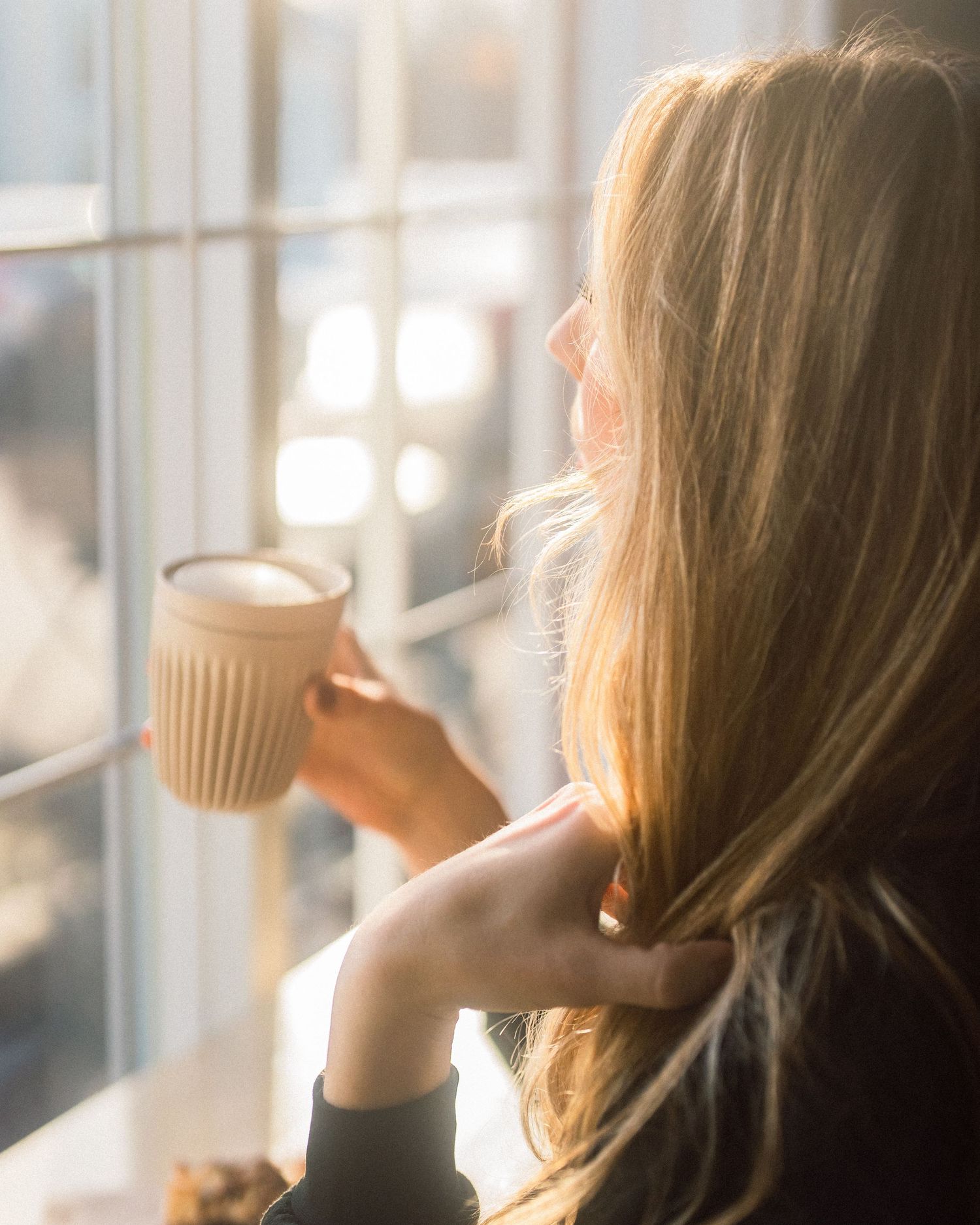 Woman enjoying a peaceful morning coffee by a sunlit window.