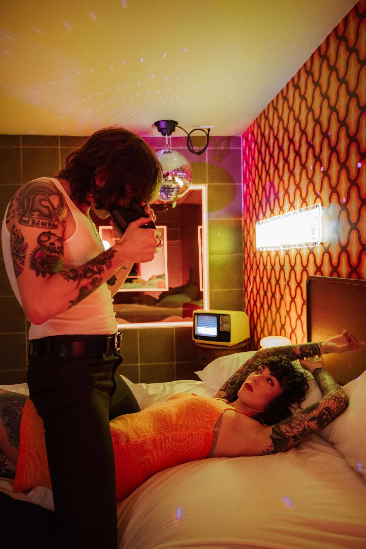 Intimate couple sharing romantic moments in a room with retro orange wallpaper and warm lighting.