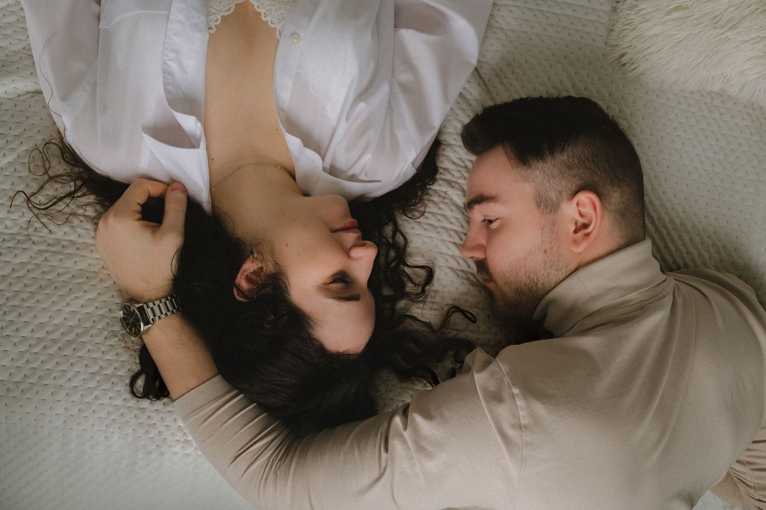 Couple lying close together on white bedding sharing an intimate moment.