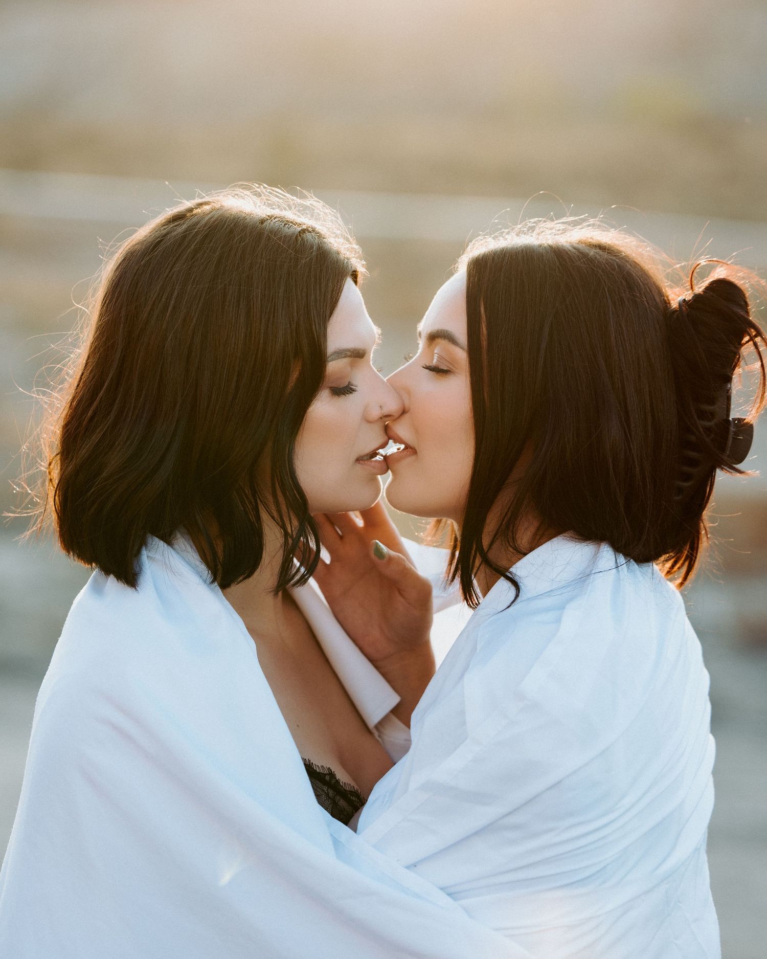 Two people wrapped in white fabric share an intimate moment at sunset.