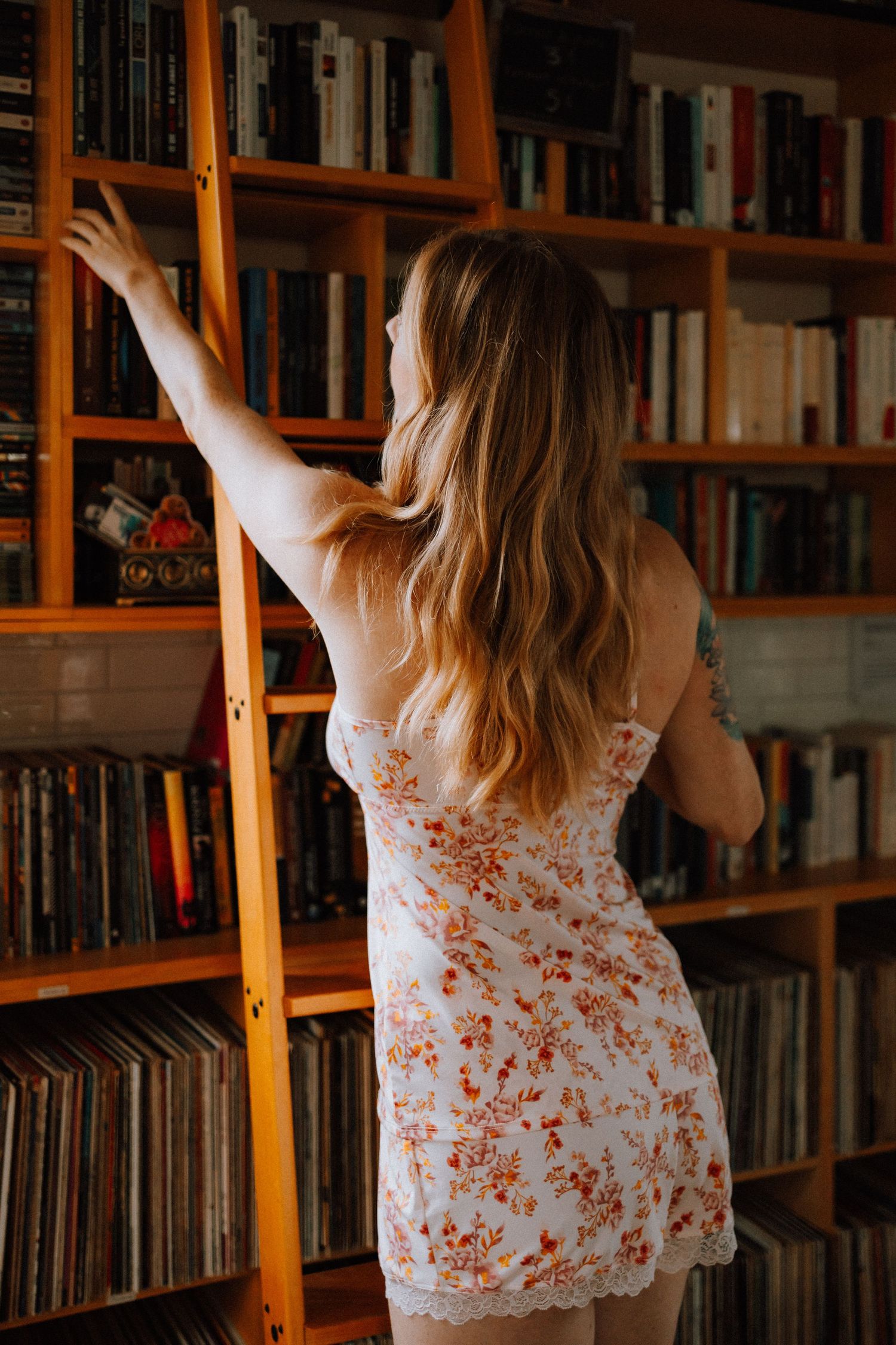 Person reaching for book on wooden shelves filled with literature.