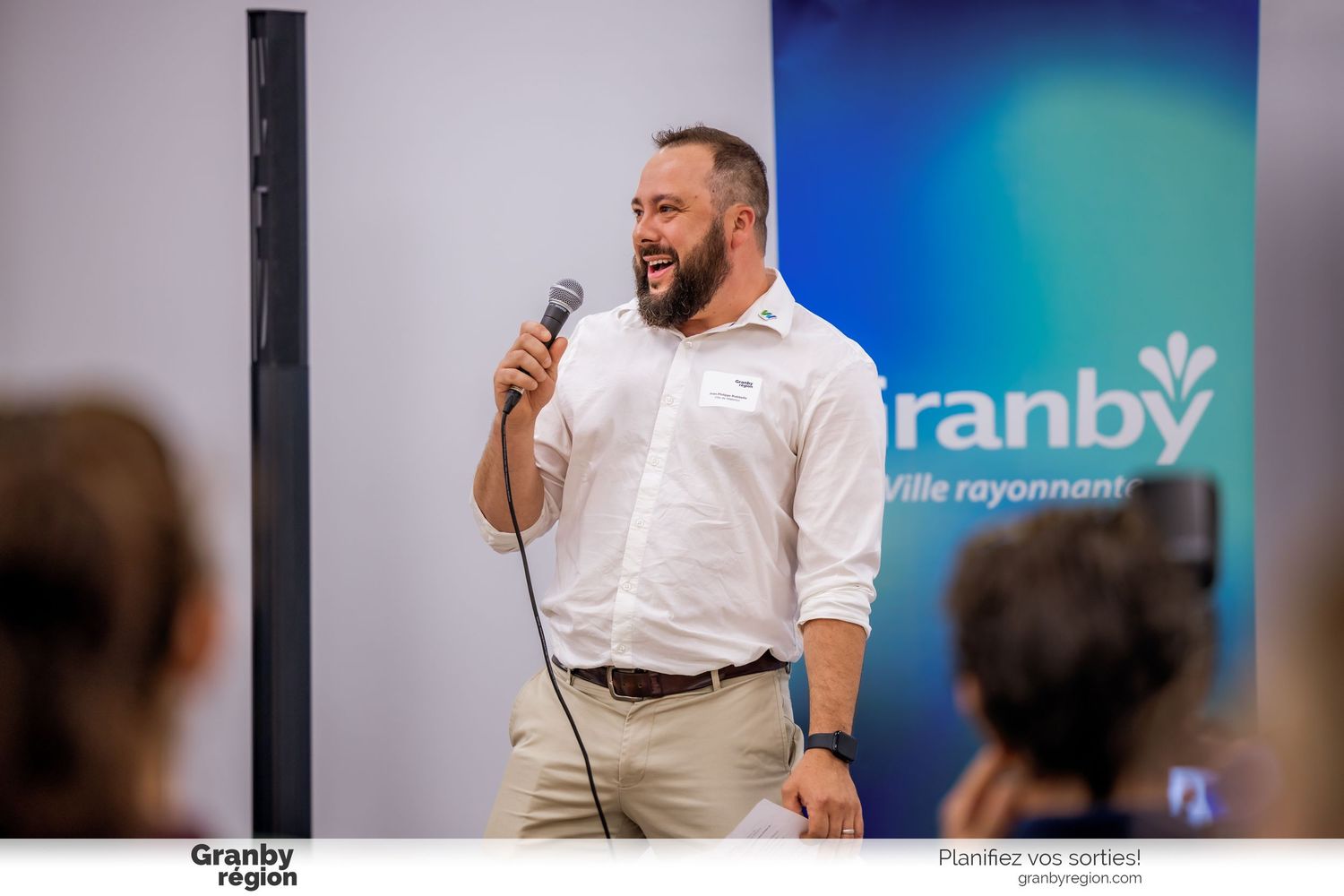 Speaker presenting to an audience against a blue gradient backdrop in a professional setting.