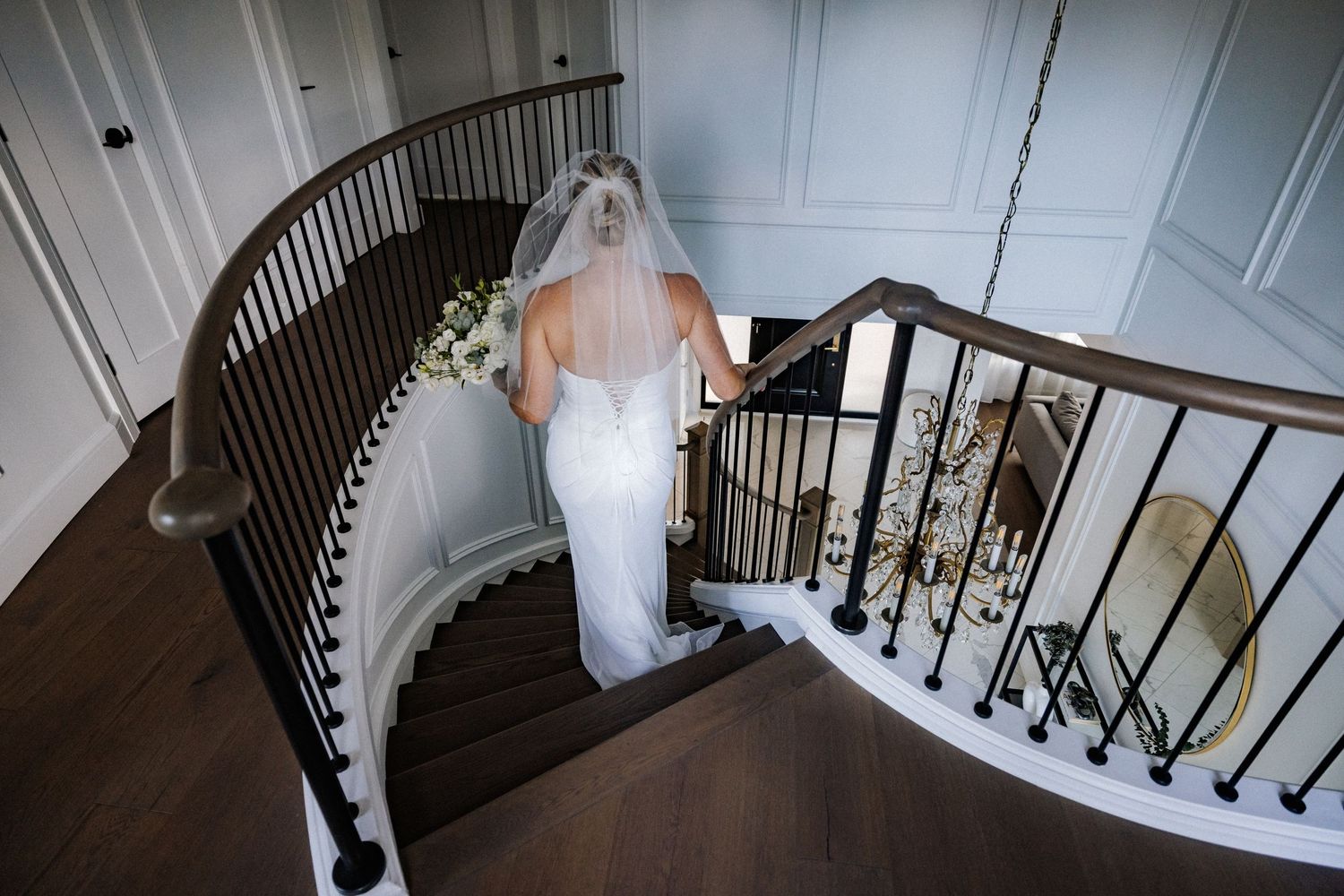 Wedding party descends elegant staircase with dark wood railings.