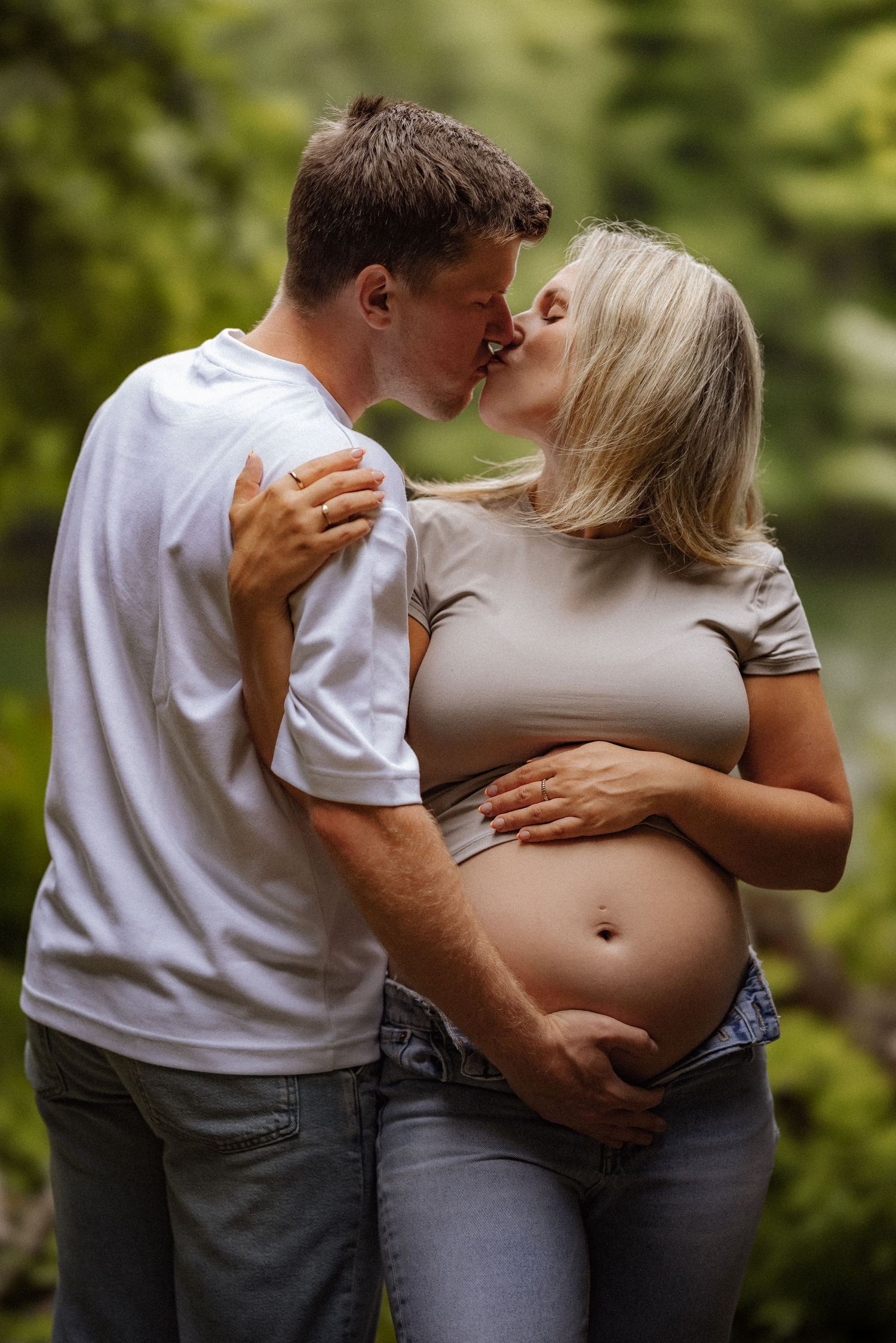 Intimate maternity photo of a couple sharing a tender kiss outdoors with her exposed pregnant belly.