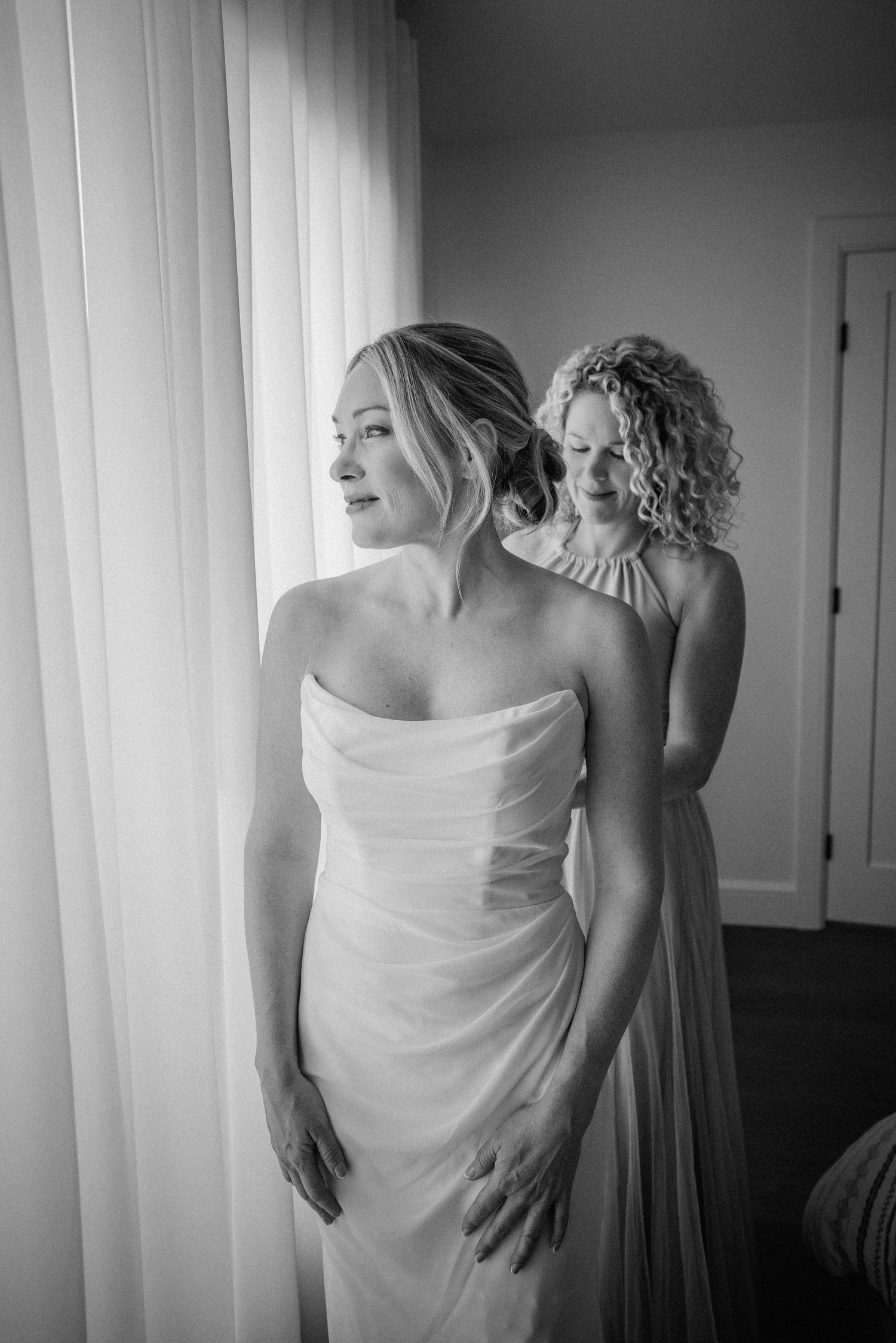 Black and white photo of wedding preparation in front of sunlit window.