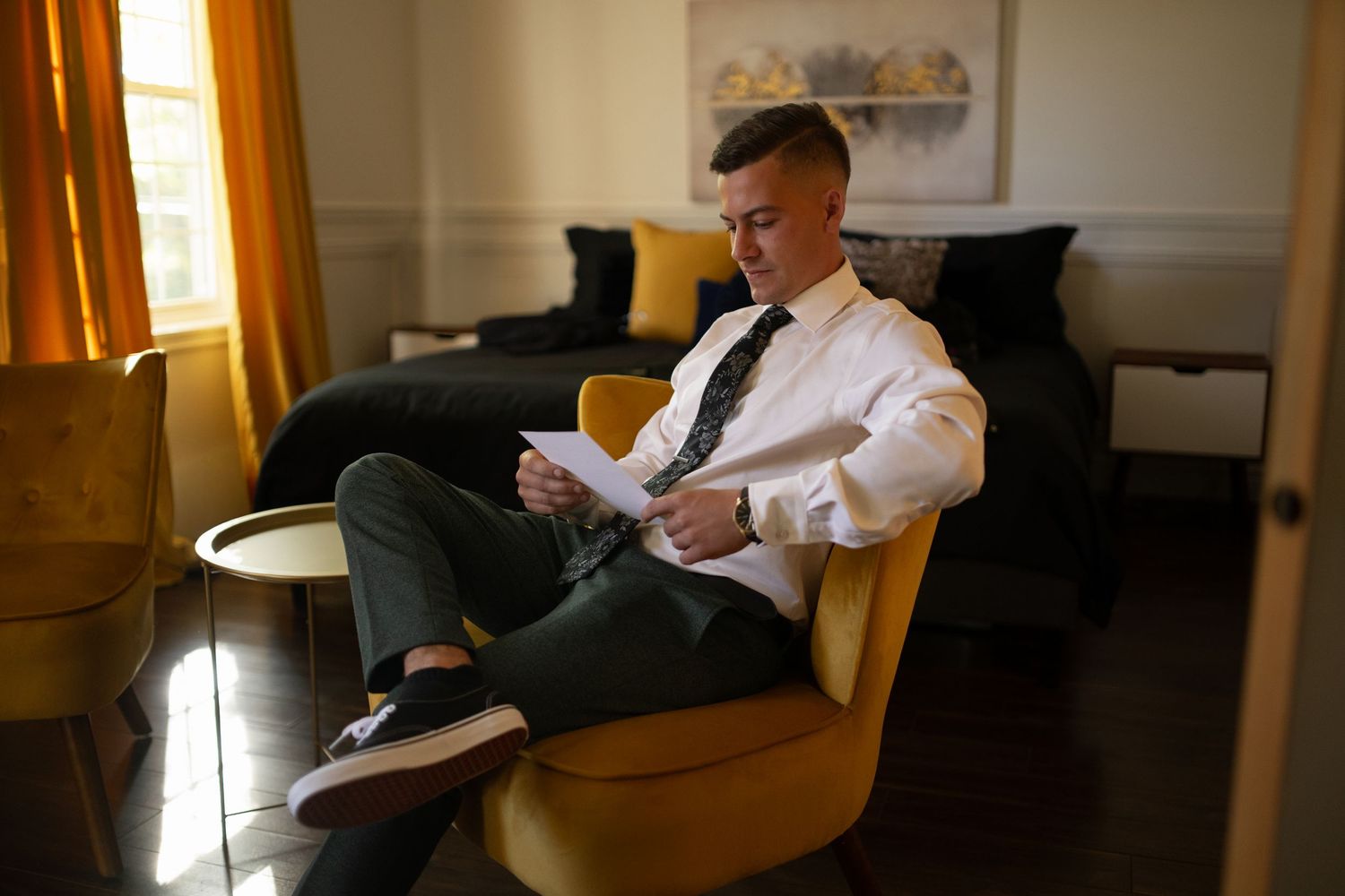 Person in formal attire sitting in yellow armchair reading papers in modern room.