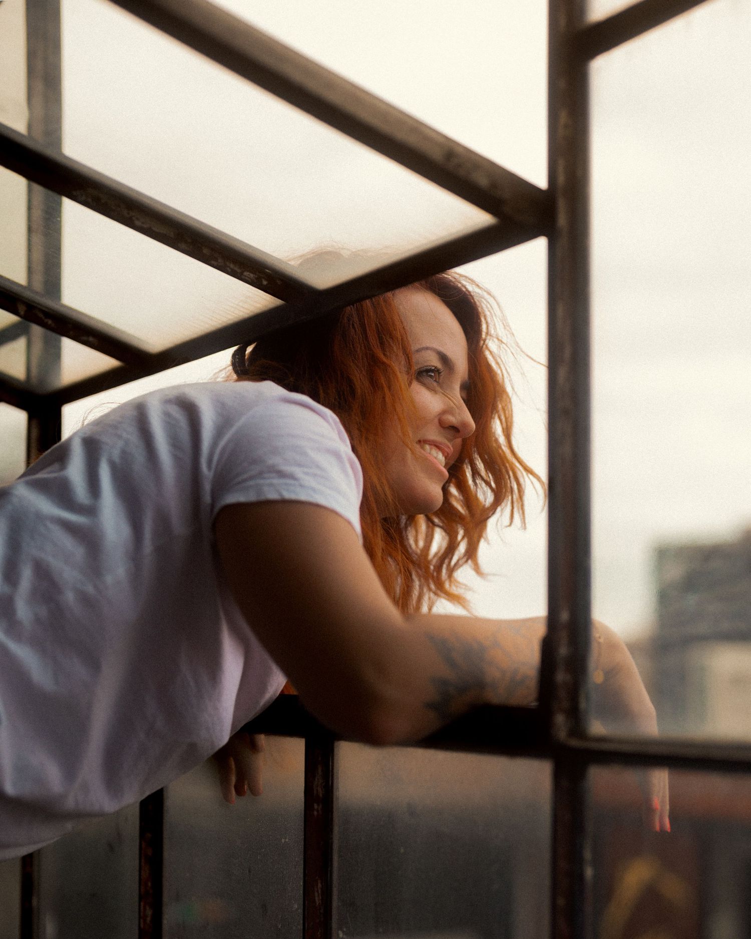 Person with red hair resting against window bars in soft natural lighting.
