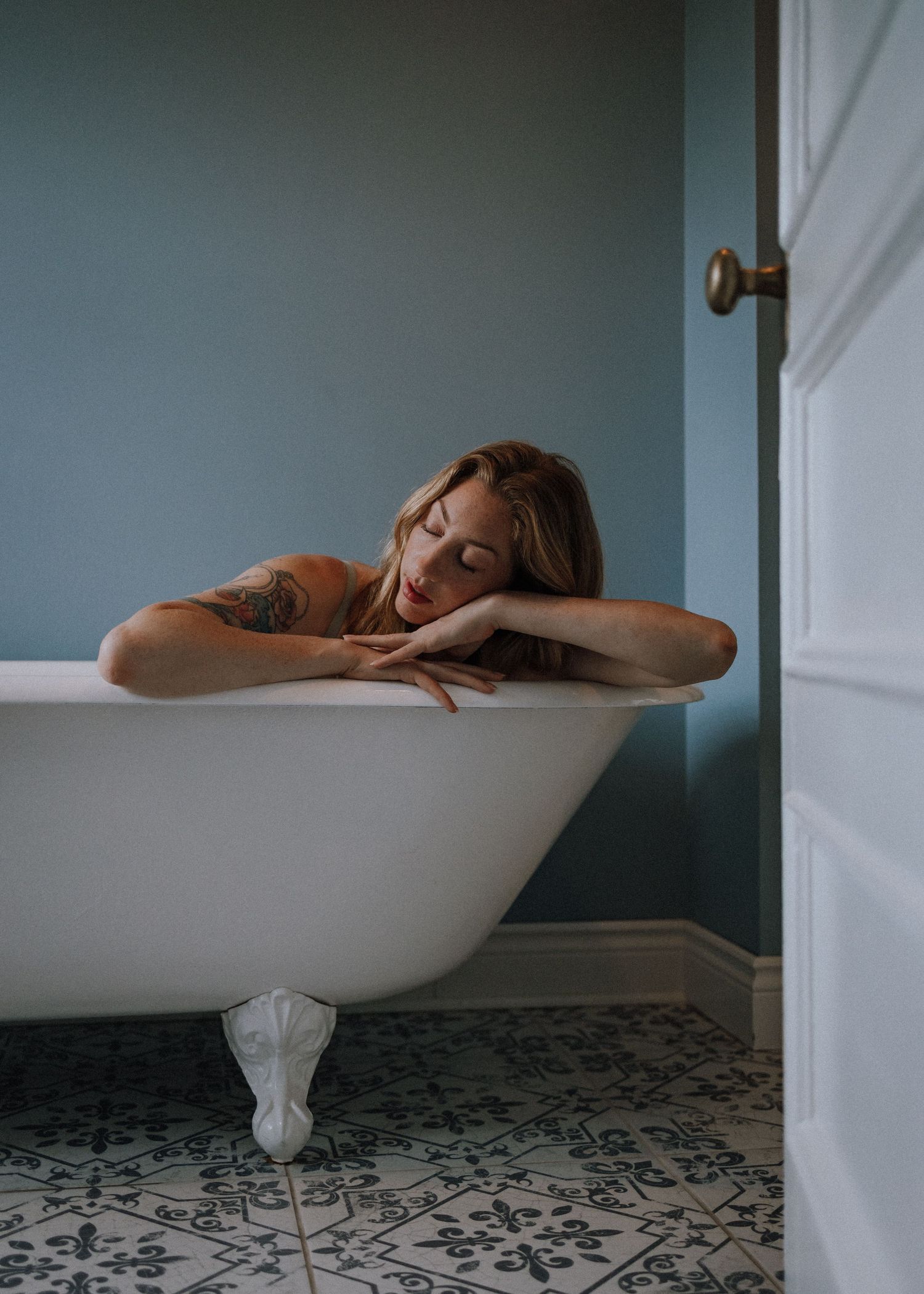 Person resting on edge of clawfoot bathtub against blue wall.