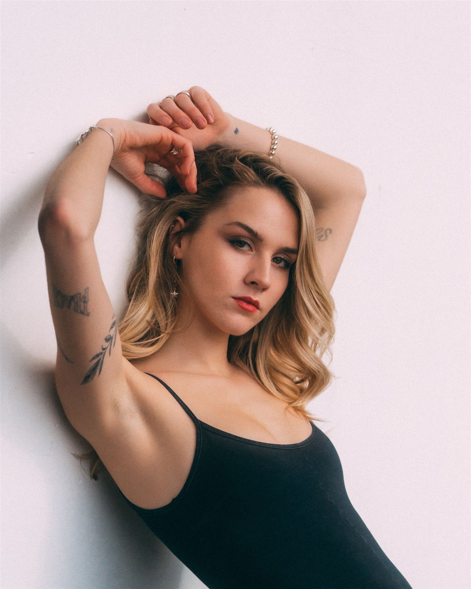 Artistic poses against white background showing tattoos and black tank top.