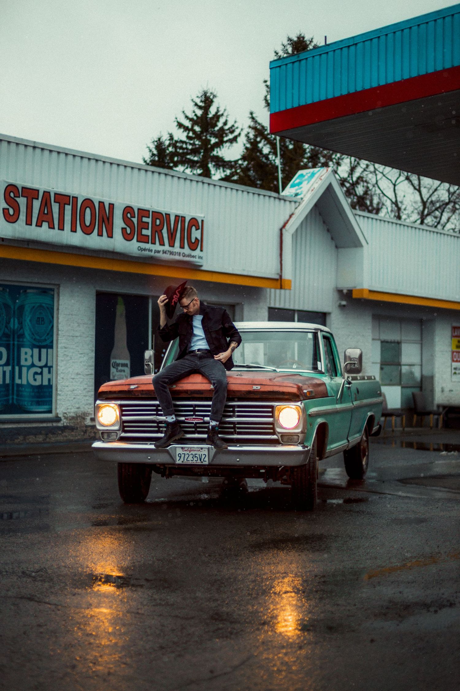 Vintage cars parked outside a retro service station on a rainy evening.