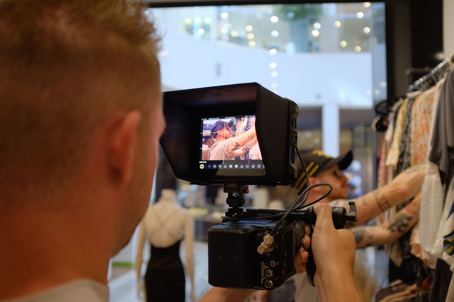 Cameraman filming through a monitor in a clothing store, capturing behind-the-scenes video production footage.