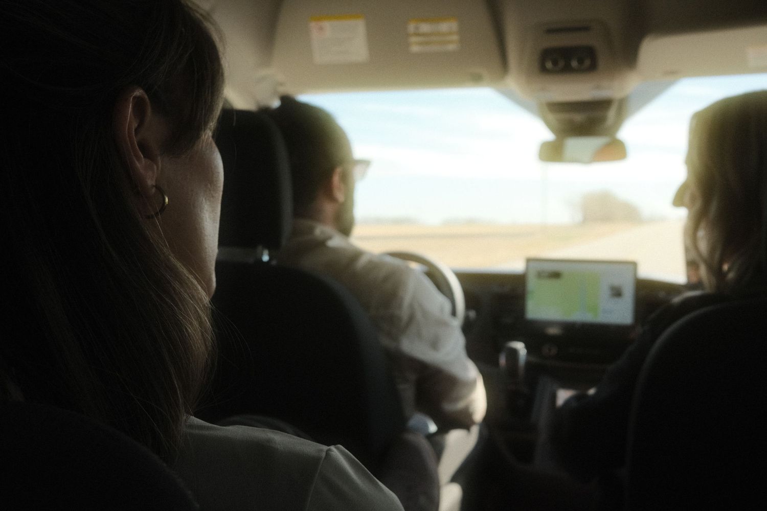 Passengers riding in a car through a desert landscape with a GPS navigation screen visible on the dashboard.