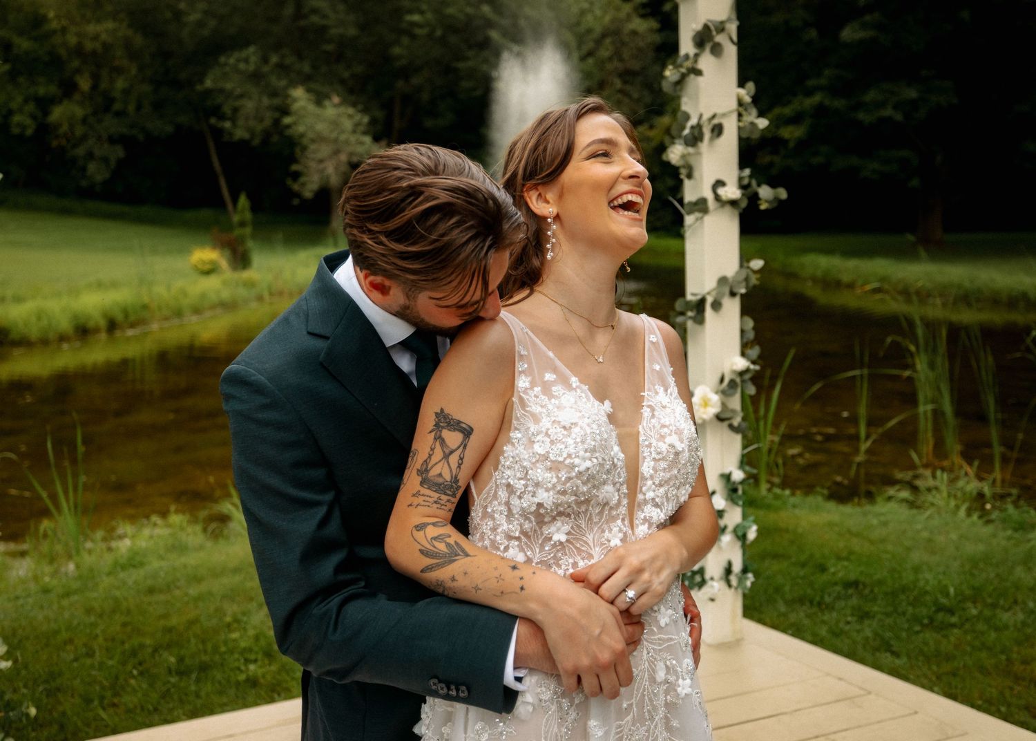 A romantic moment captured between newlyweds by a pond with white columns in the background.