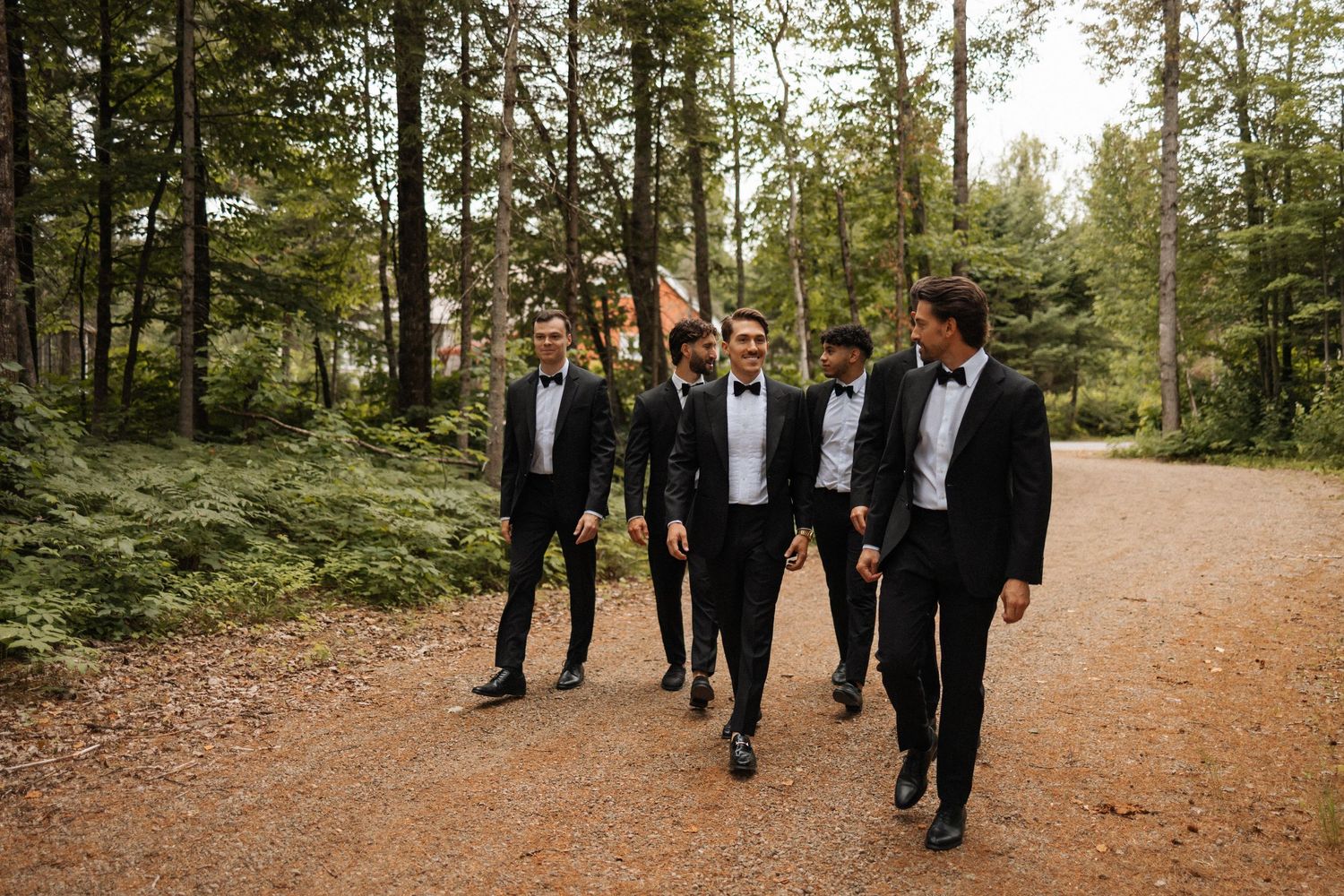 Wedding party walking along a forest trail in formal black attire.