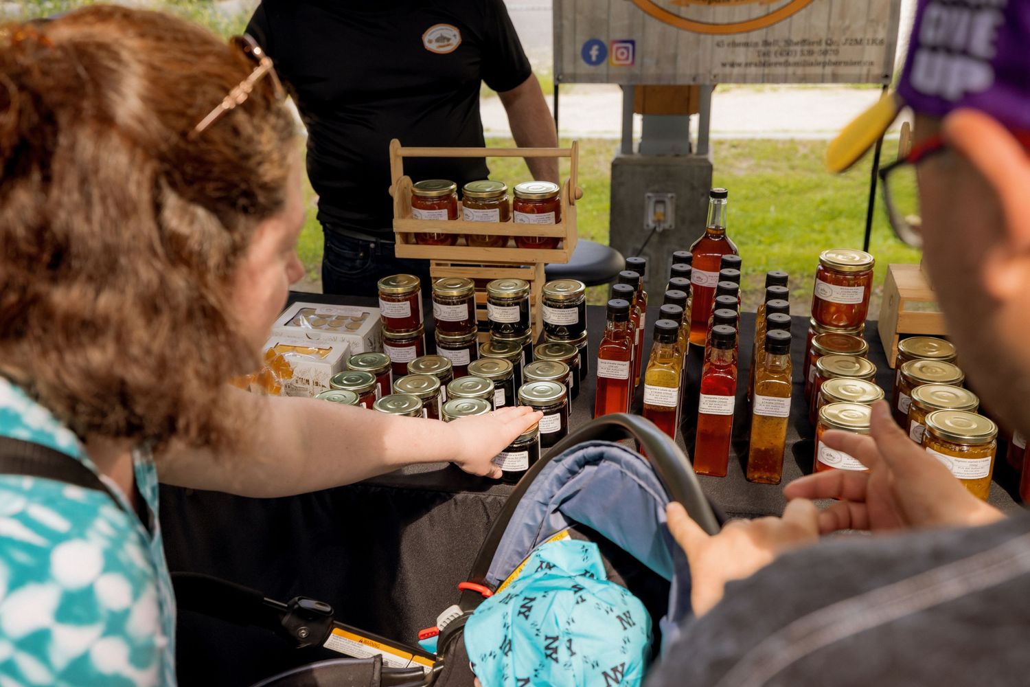 Vendor displays various sauce or condiment bottles at an outdoor market stall.