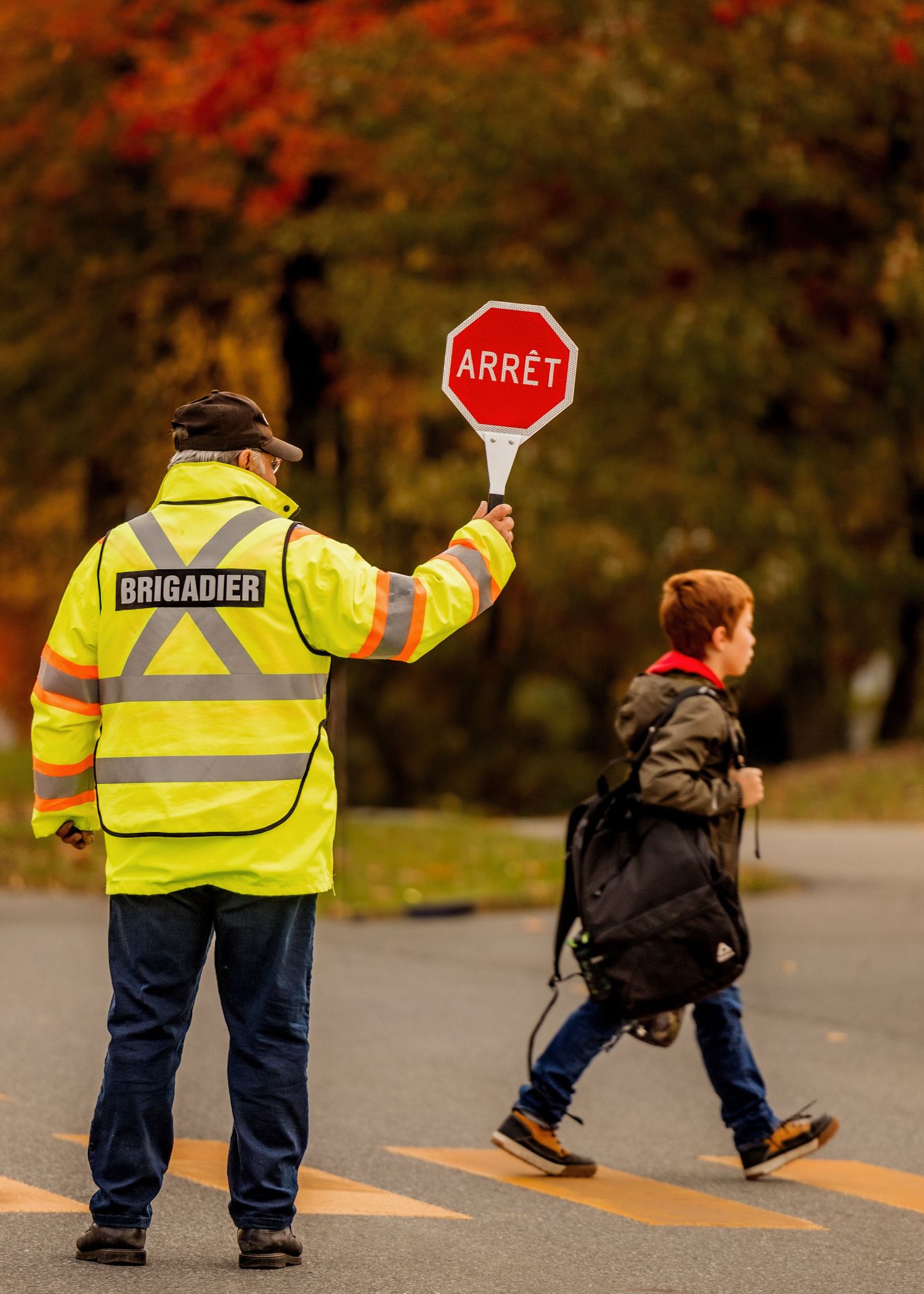 Crossing guard in reflective vest helping pedestrians cross a street in autumn.