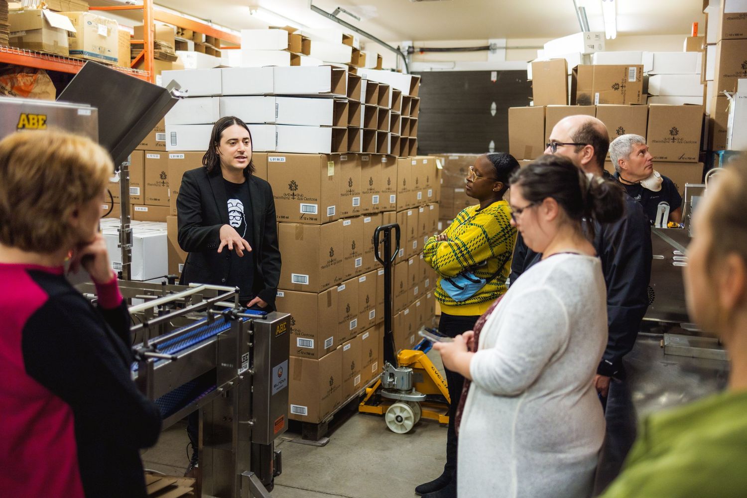 People exploring a warehouse storage area filled with stacked cardboard boxes and supplies.