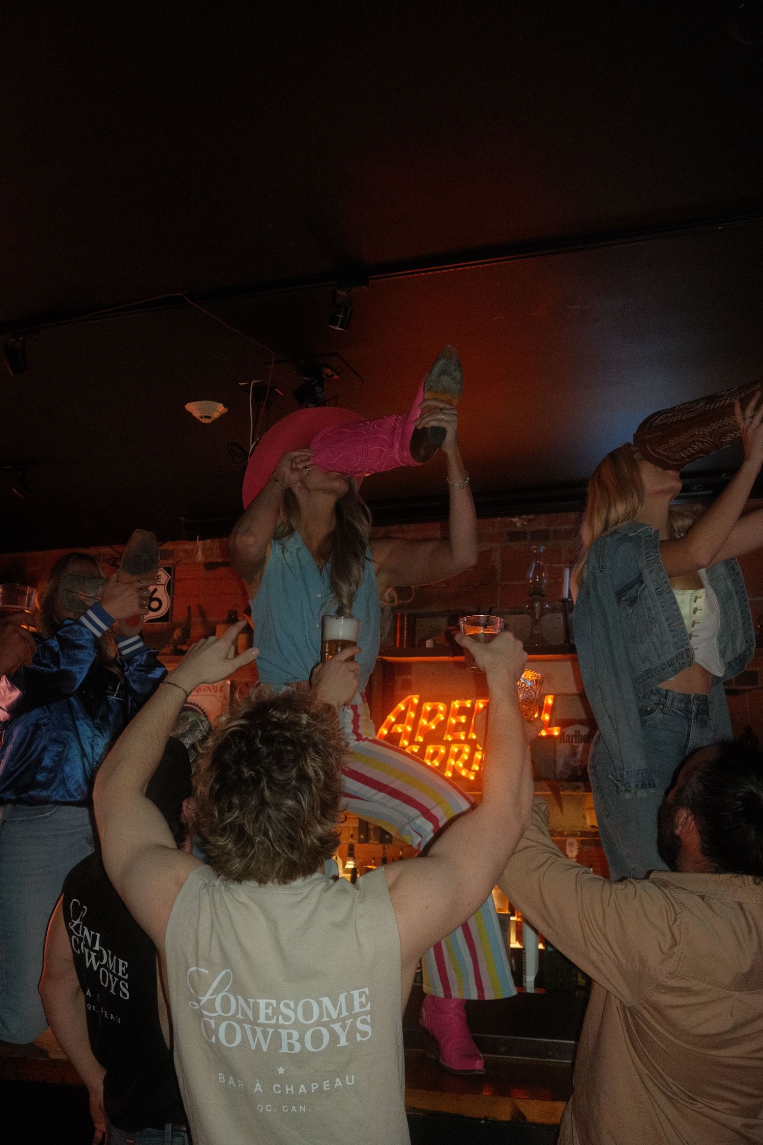 People dancing and celebrating at Lonesome Cowboys bar, with a woman in pink being lifted above the crowd.