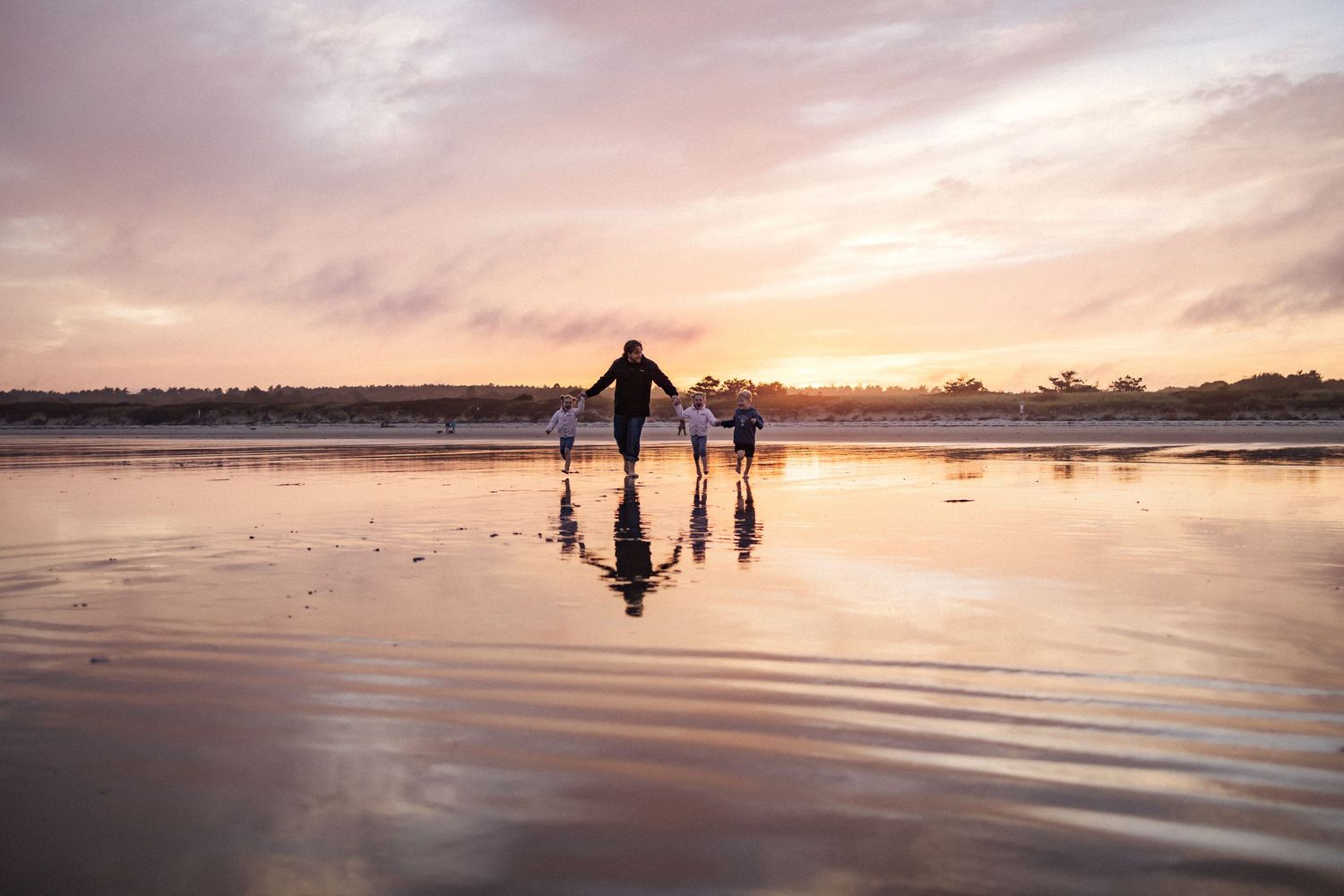 People walking on reflective wet sand during a colorful beach sunset.