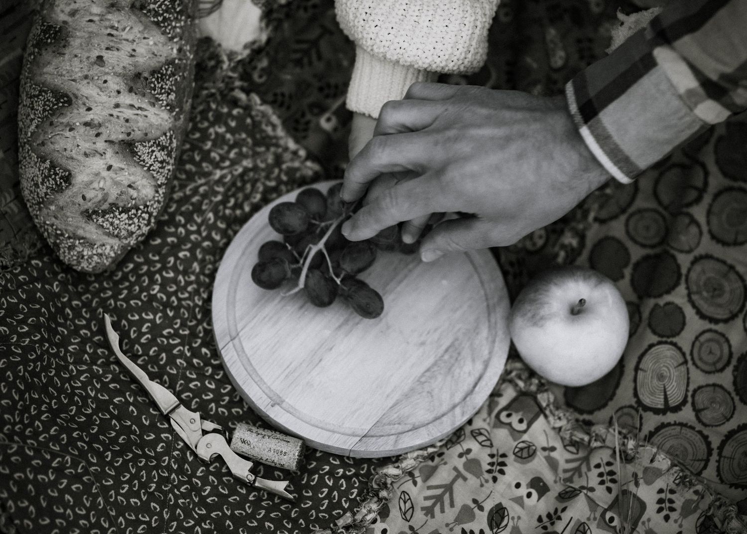 Black and white close-up of hands carving a pumpkin with autumn decor nearby.