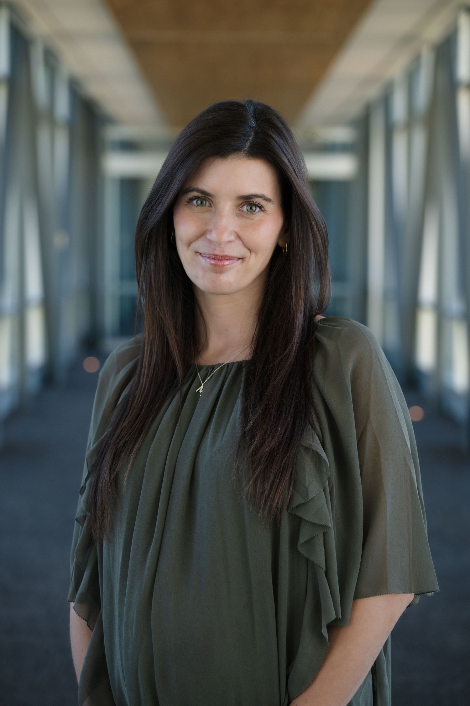 Professional portrait in modern hallway with glass windows and industrial ceiling.