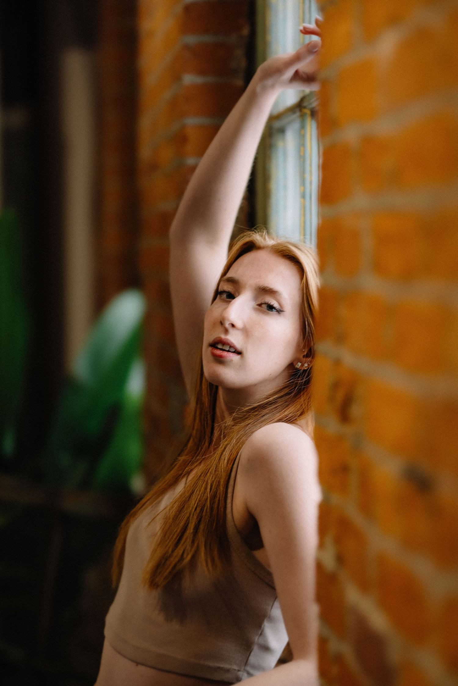 Person in brown top poses gracefully against brick wall in warm lighting.