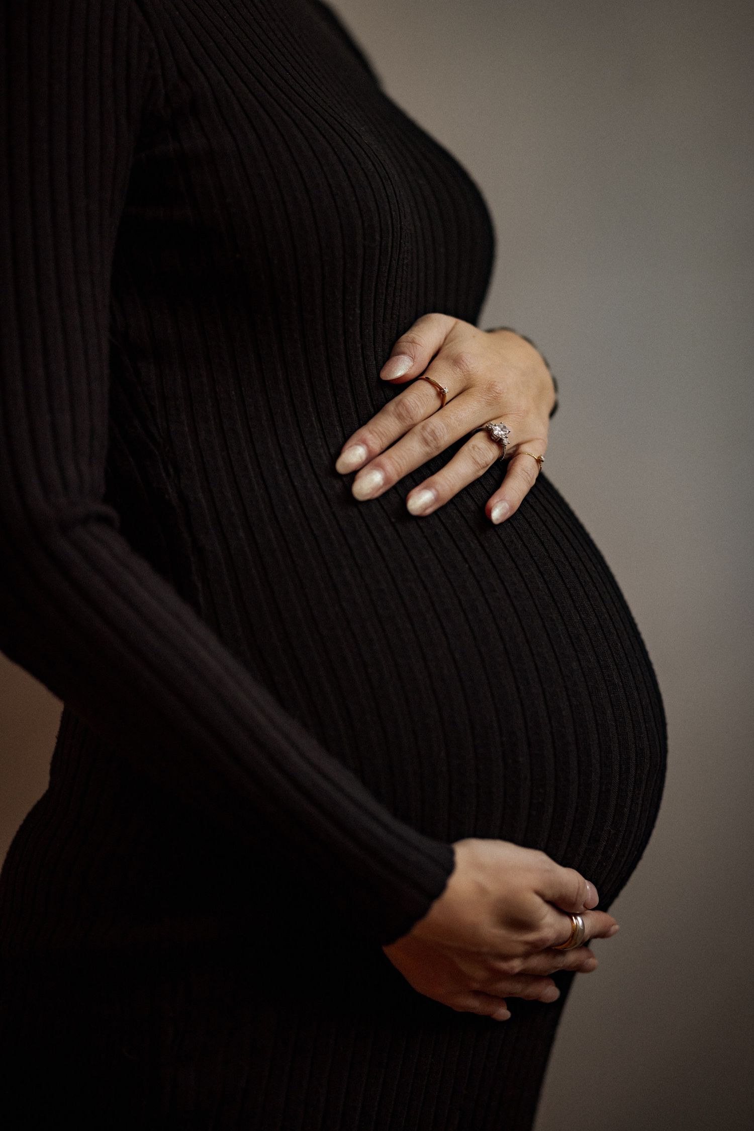 Close-up shots of a pregnant belly in a black ribbed dress with hands showing wedding ring.