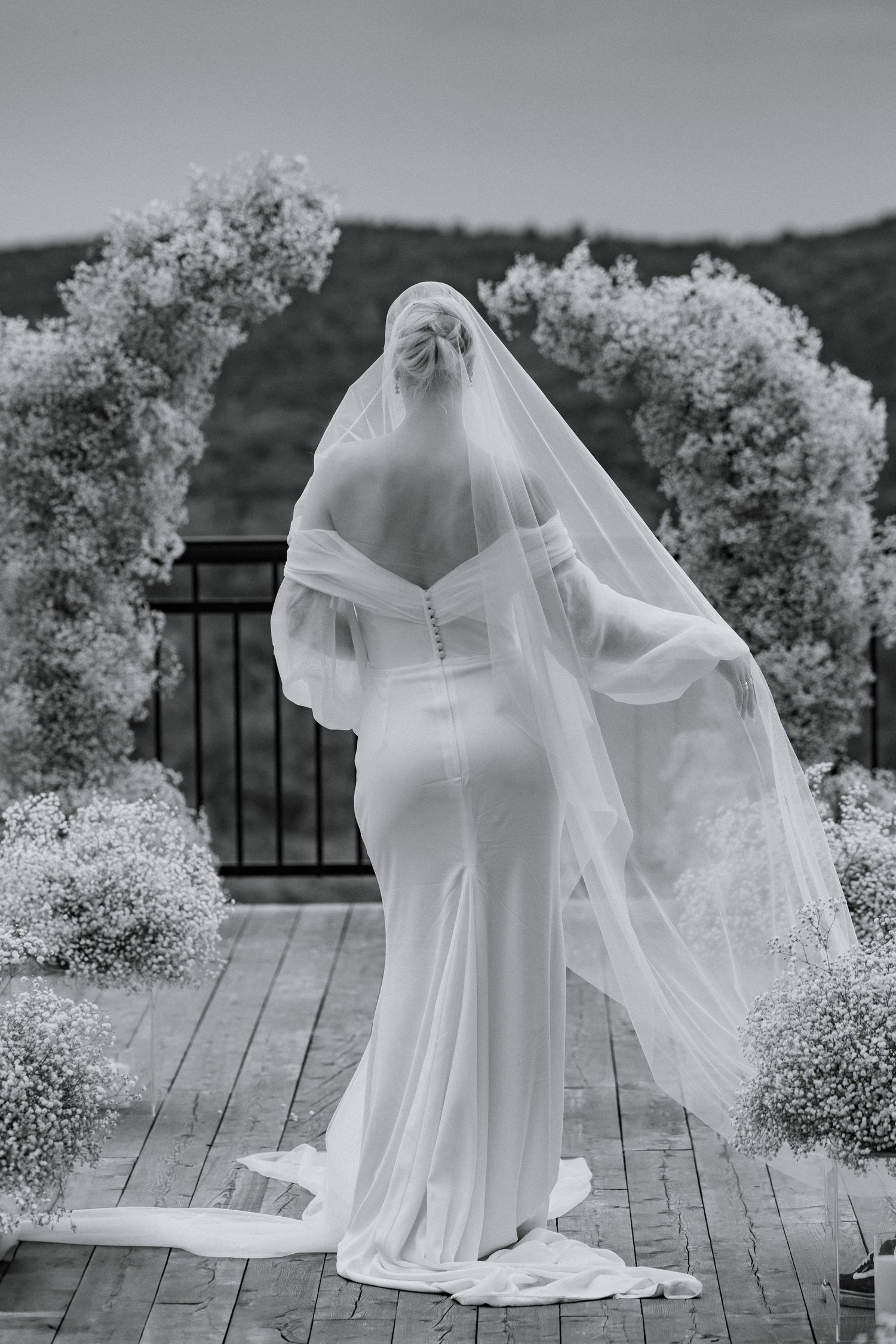 Black and white portrait of wedding dress with ethereal veil on mountain deck.