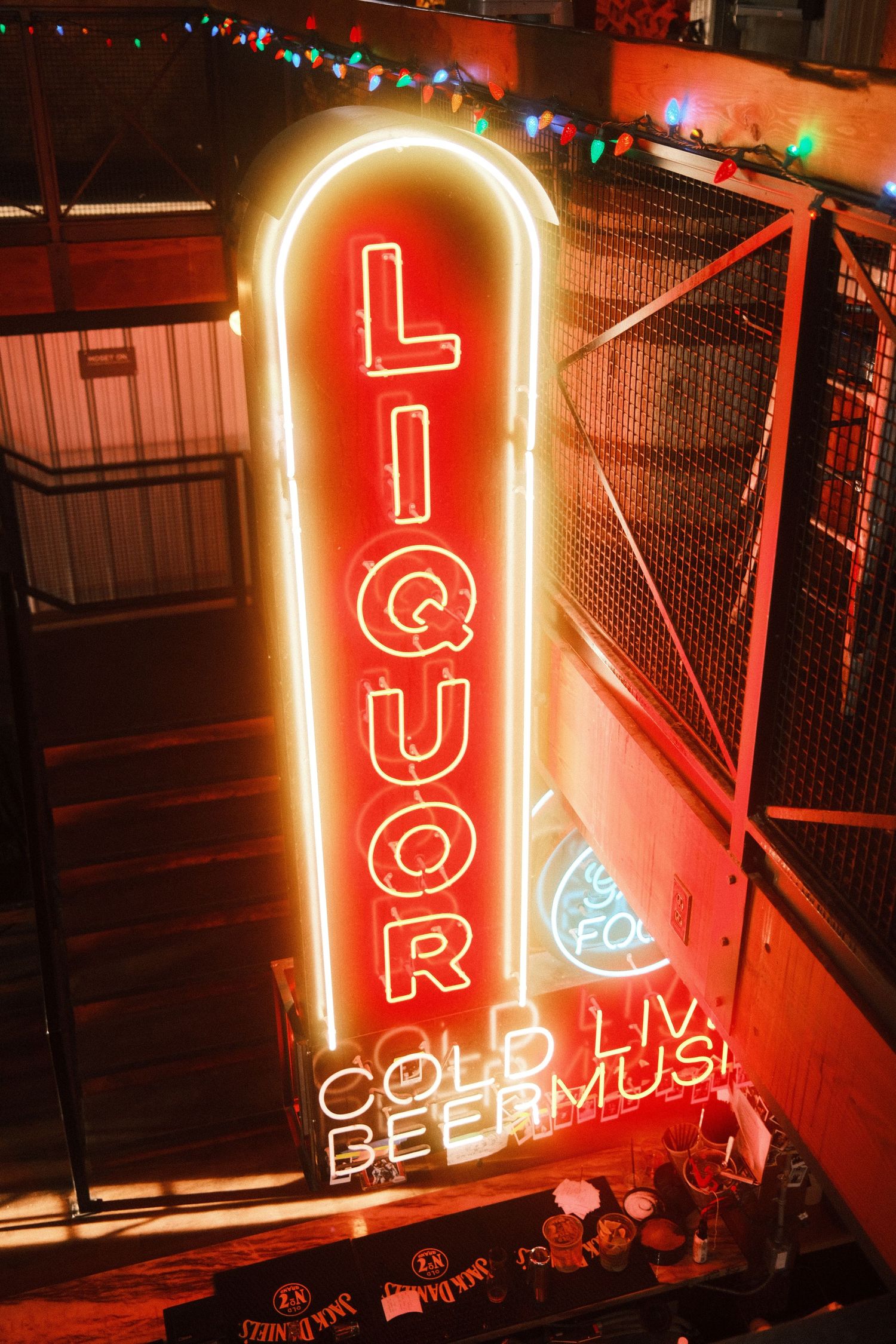 Vintage neon liquor sign glowing red and white, advertising cold beer and live music in a bar setting.