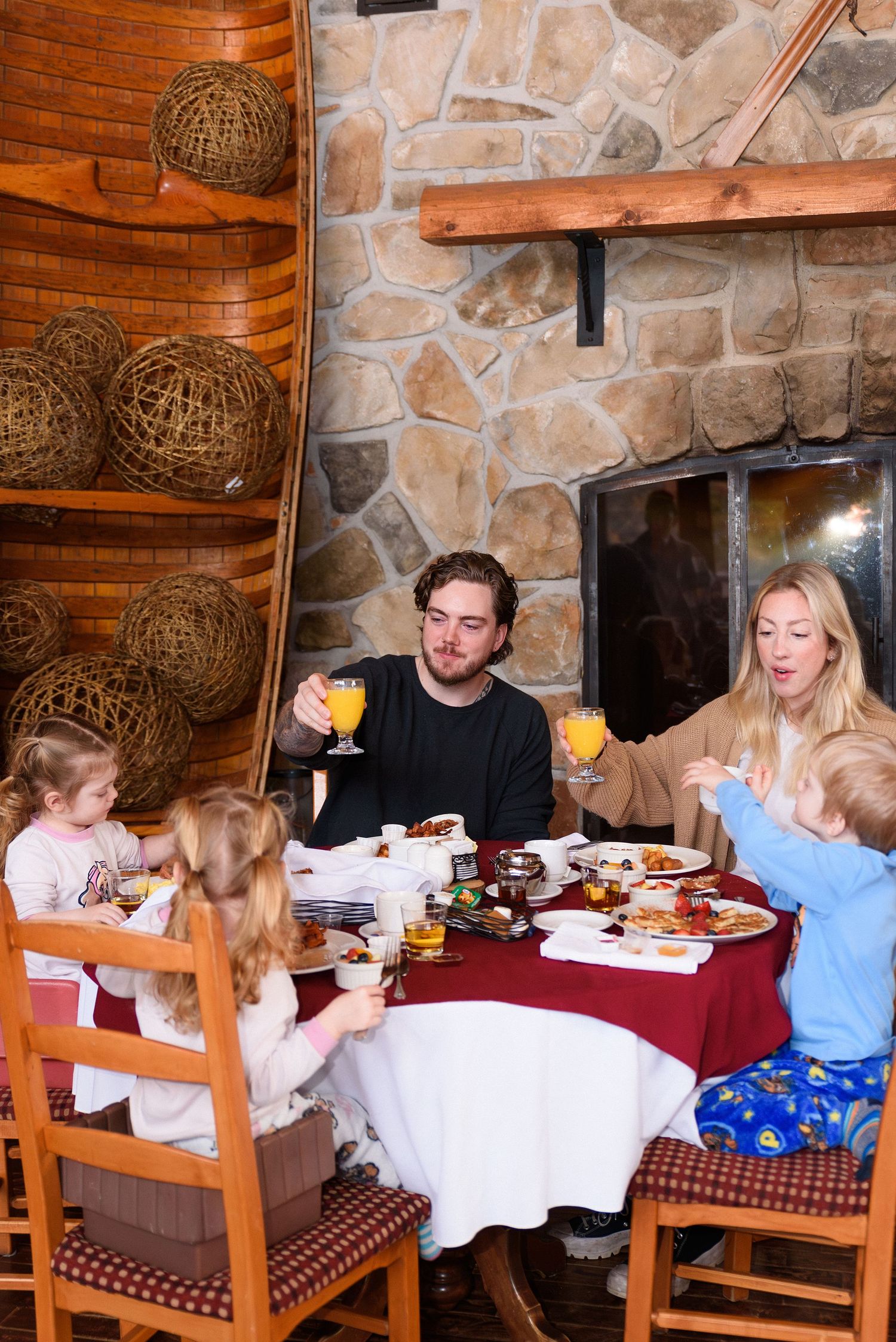 Family dining together at a rustic stone-walled restaurant, toasting with orange juice glasses over a festive meal.