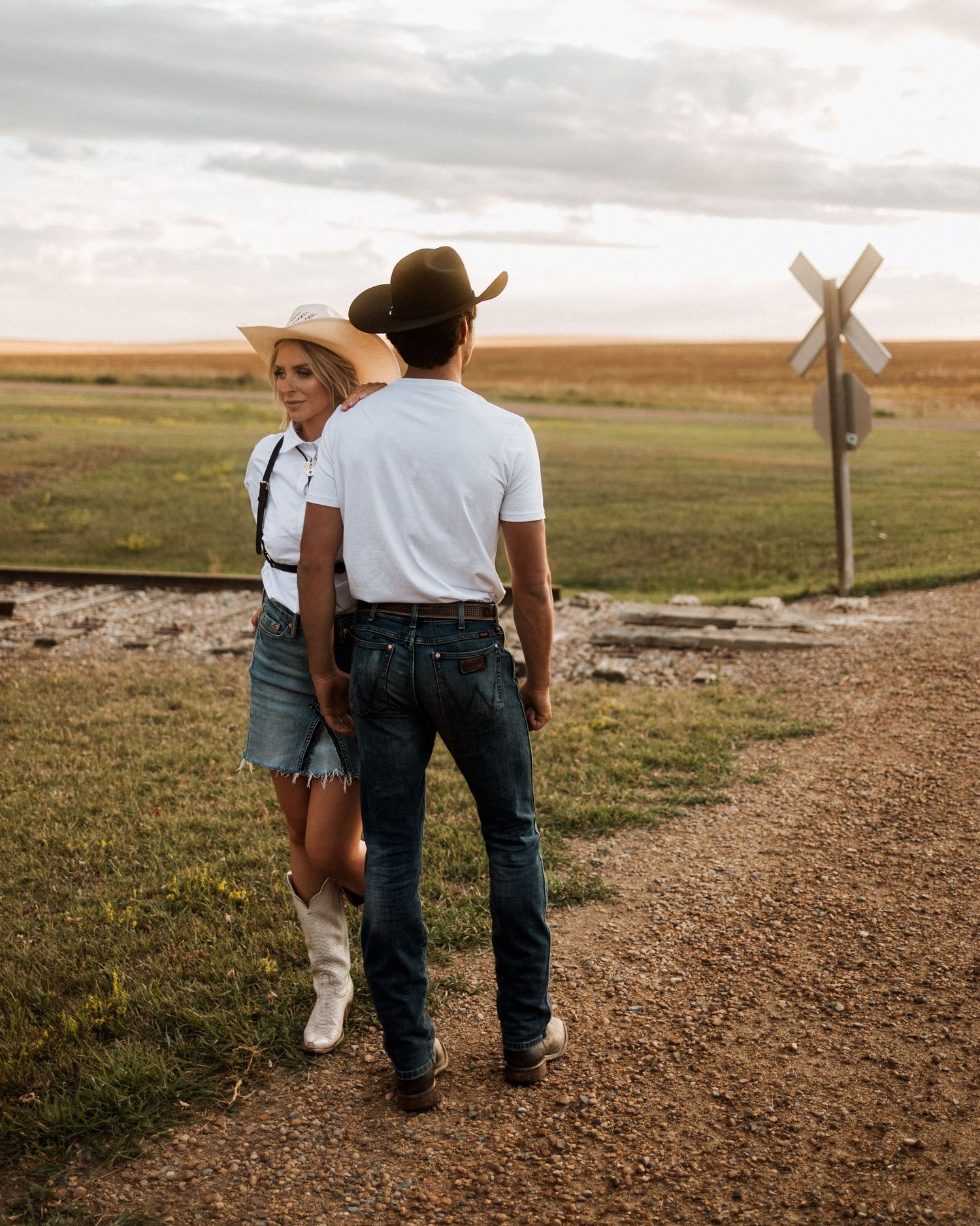 Couple in western wear walking together on a dirt path at sunset.