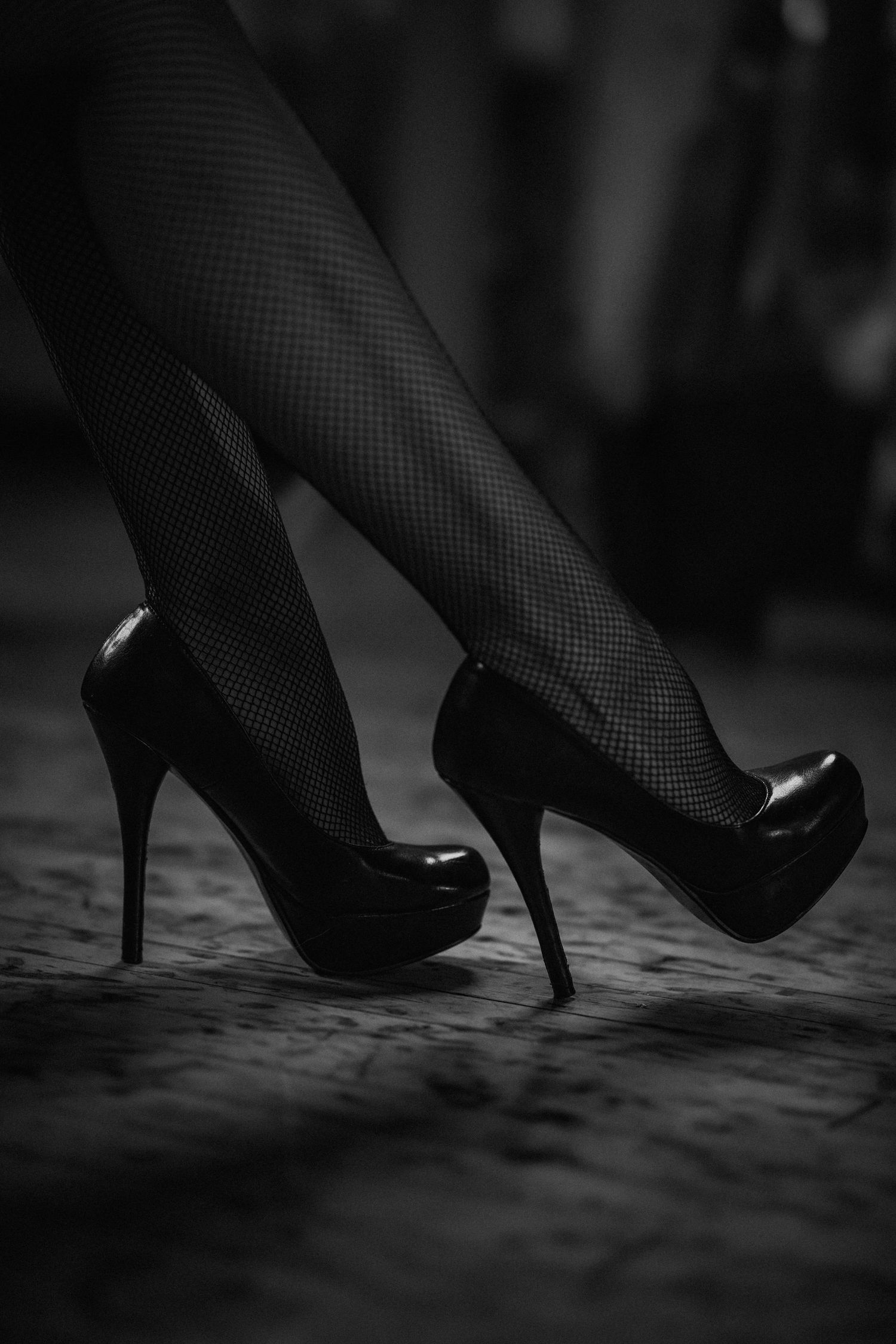Close-up of black high heels walking on textured surface in dramatic lighting.