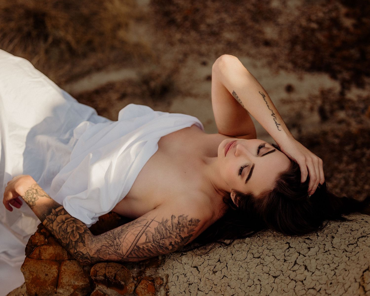 A figure in a flowing white dress poses gracefully against a rustic backdrop.