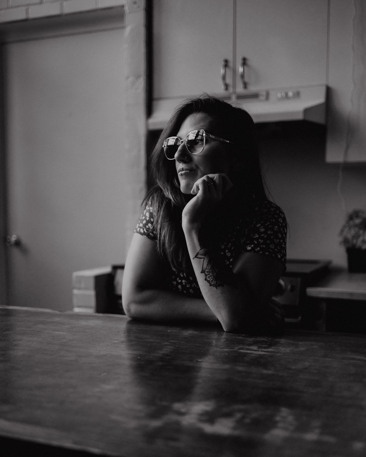 Person resting head on hand at wooden table in black and white portrait.