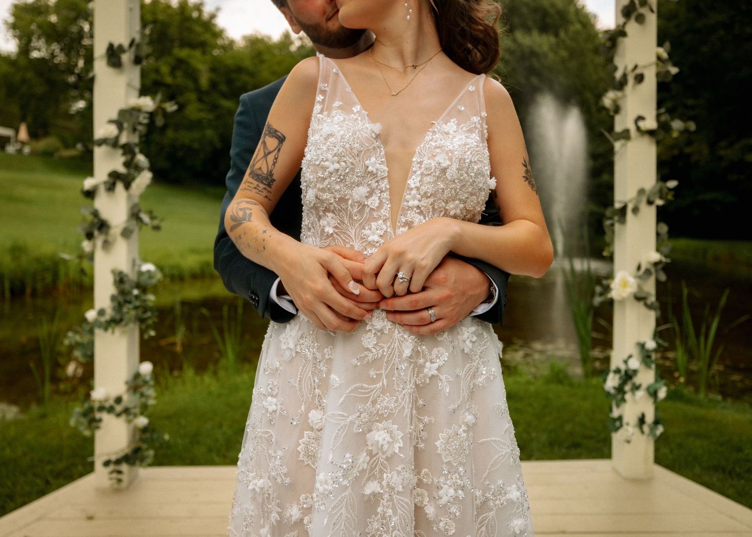 An elegant lace wedding dress with plunging neckline photographed against white columns outdoors.