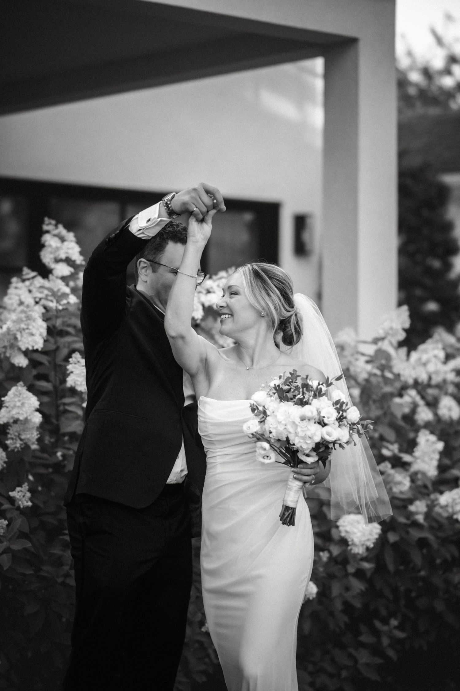 Black and white photo of couple dancing among flowering bushes at wedding.
