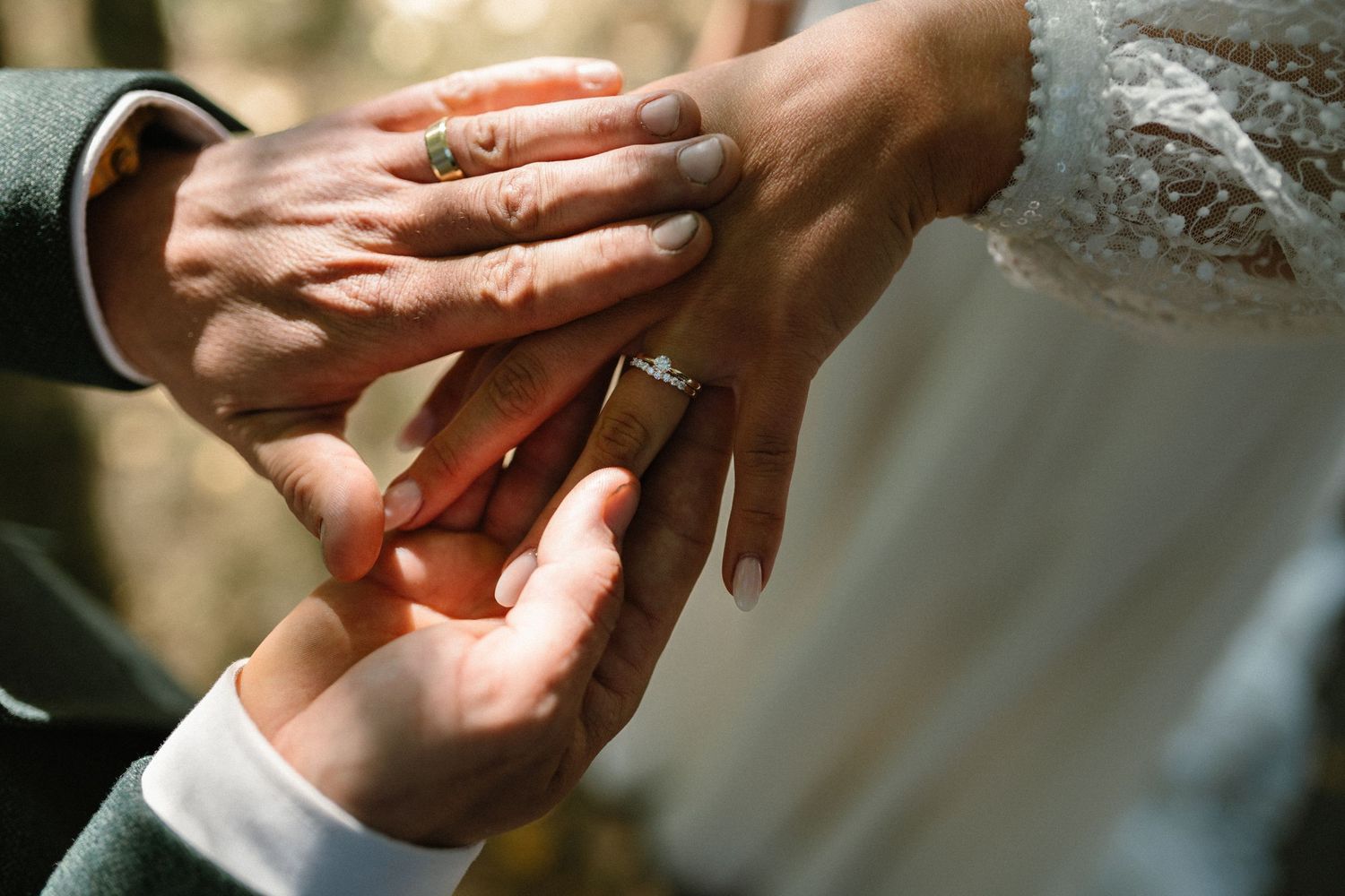 Sunlit close-up of hands during wedding ring exchange ceremony.