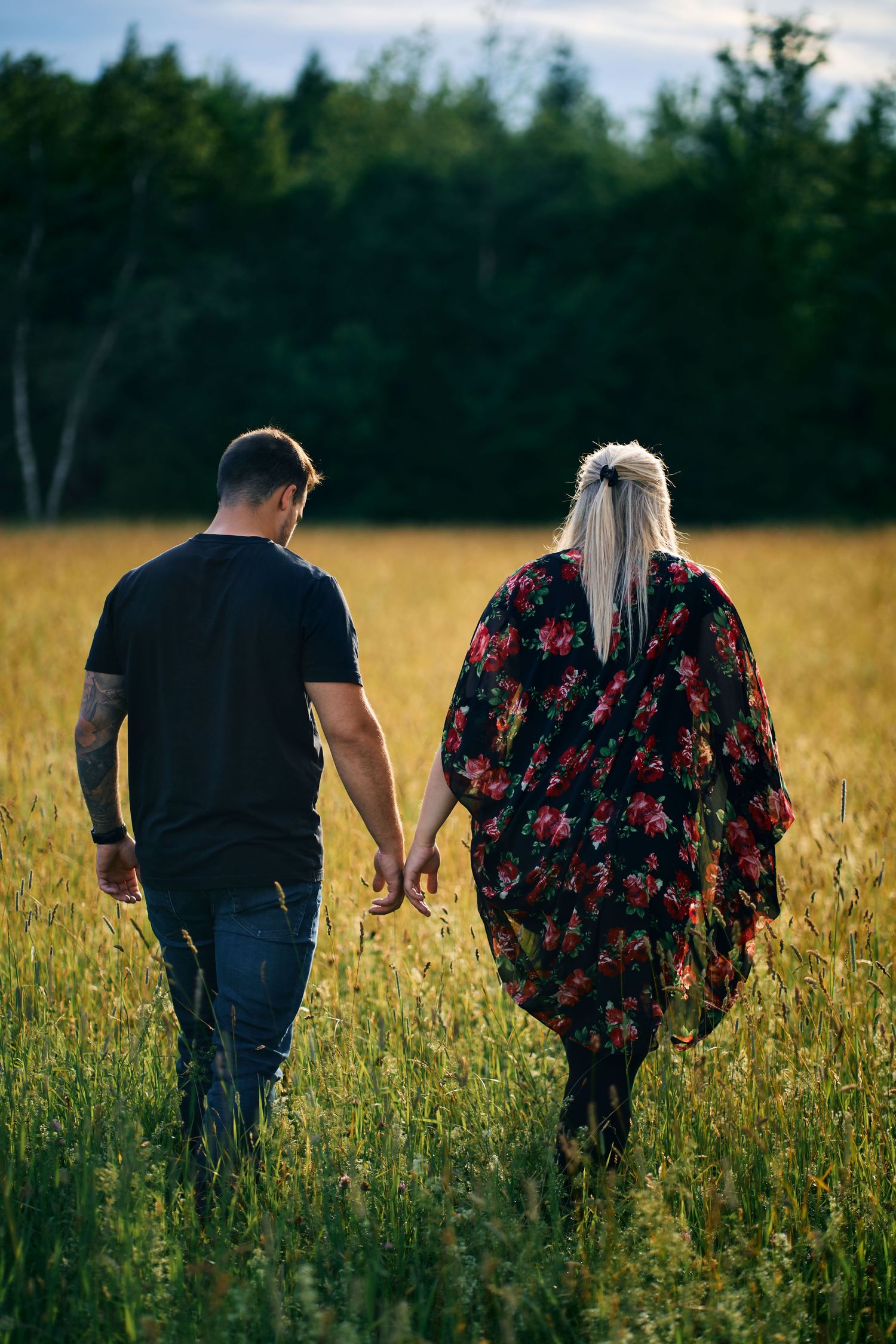 Couple walking hand in hand through a sunlit meadow with wildflowers.