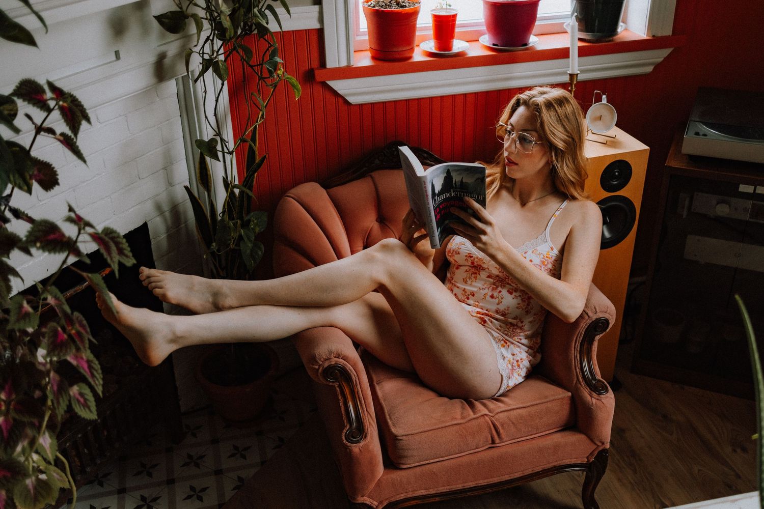 Person lounging in brown armchair with houseplants and speakers in background.