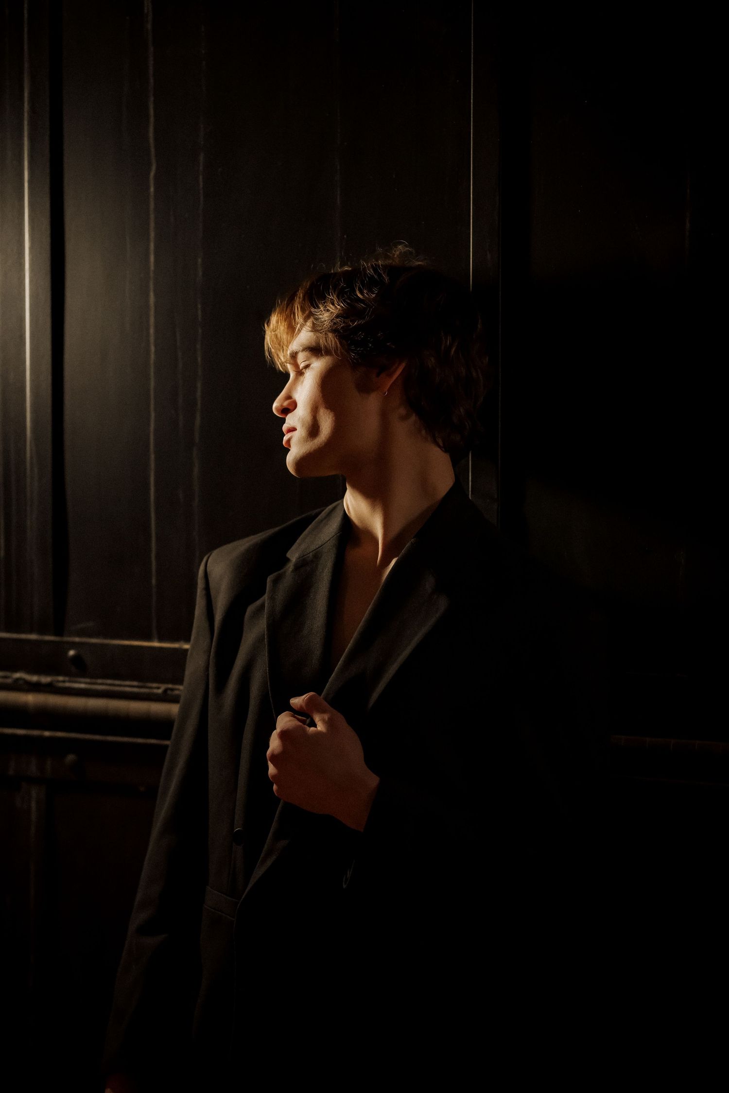 Dramatic side profile portrait in dark lighting wearing formal jacket.