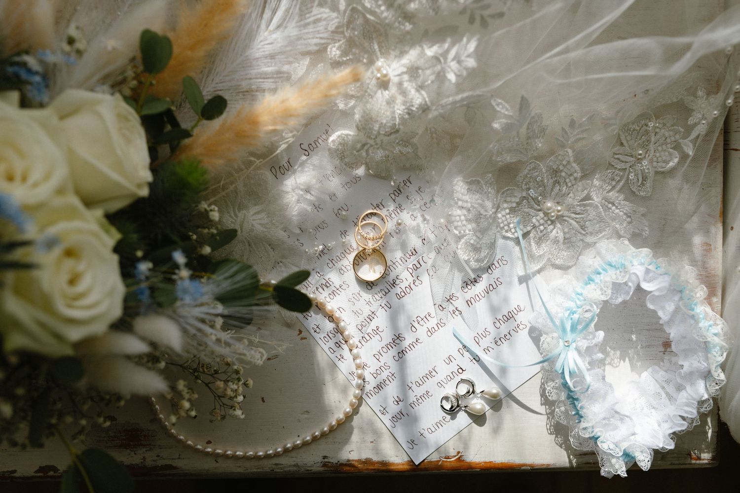 Wedding rings displayed on lace fabric with white roses and decorative elements.