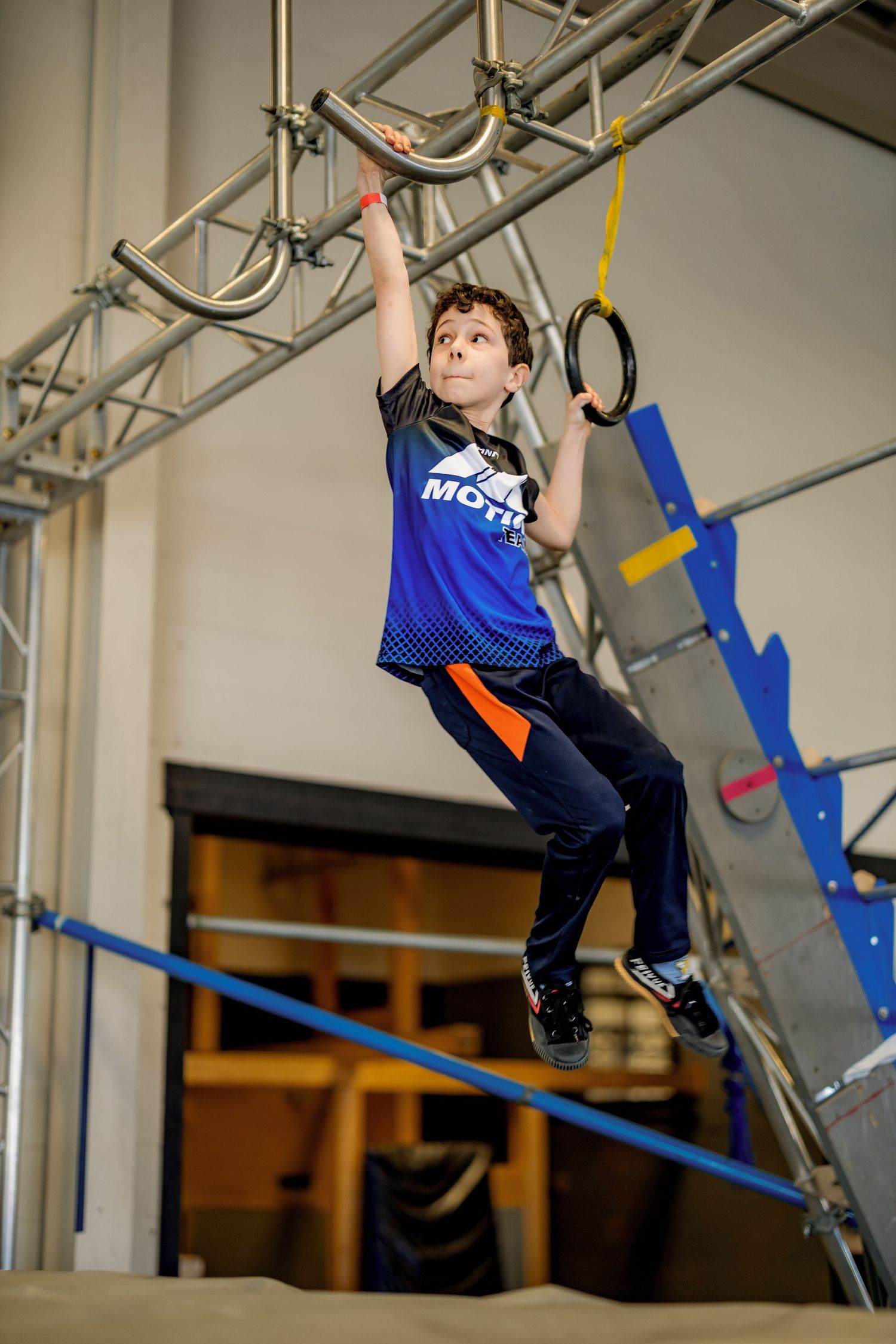 Child practicing gymnastics moves on suspended equipment in an indoor facility.