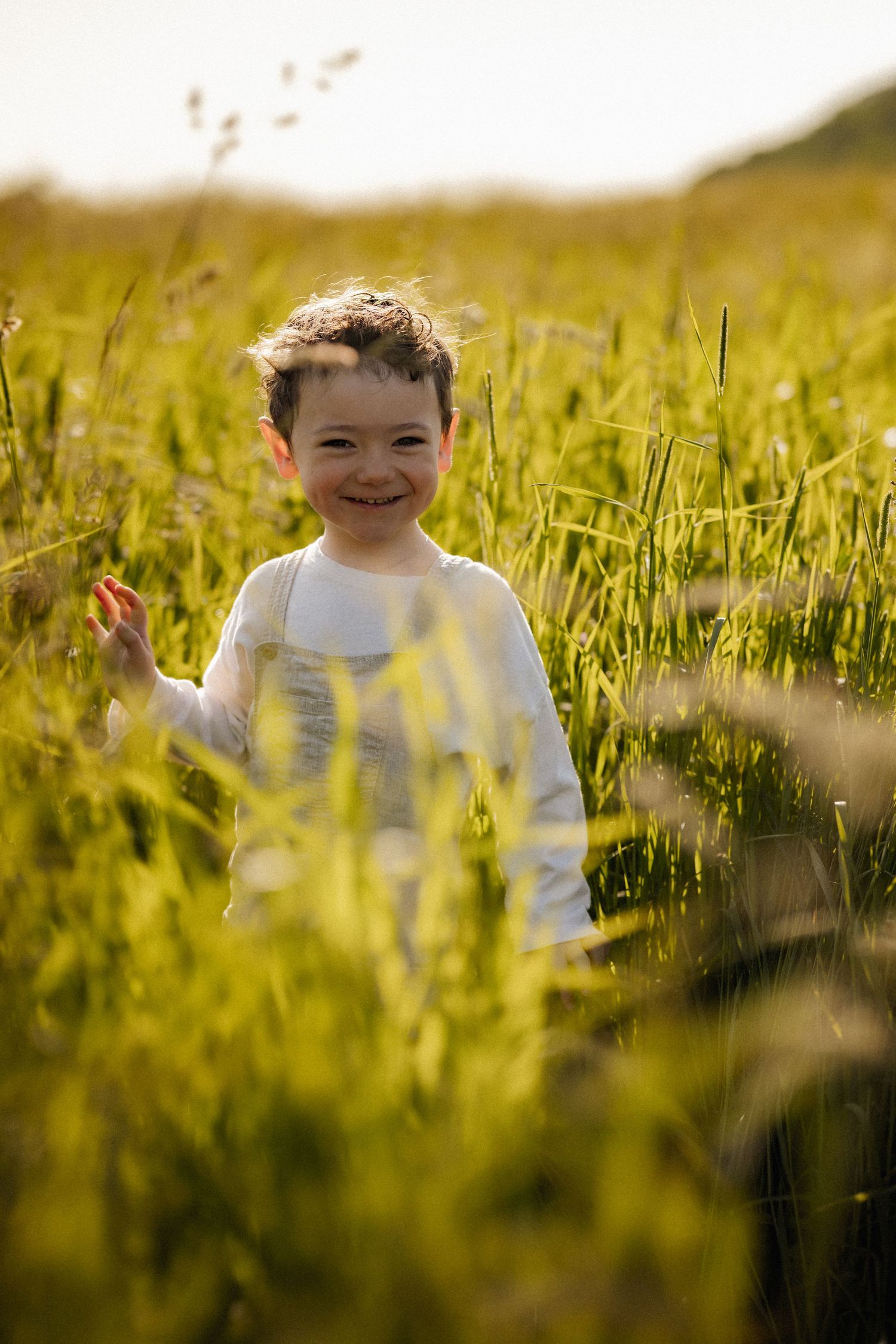 A child plays joyfully in tall grass during golden hour.